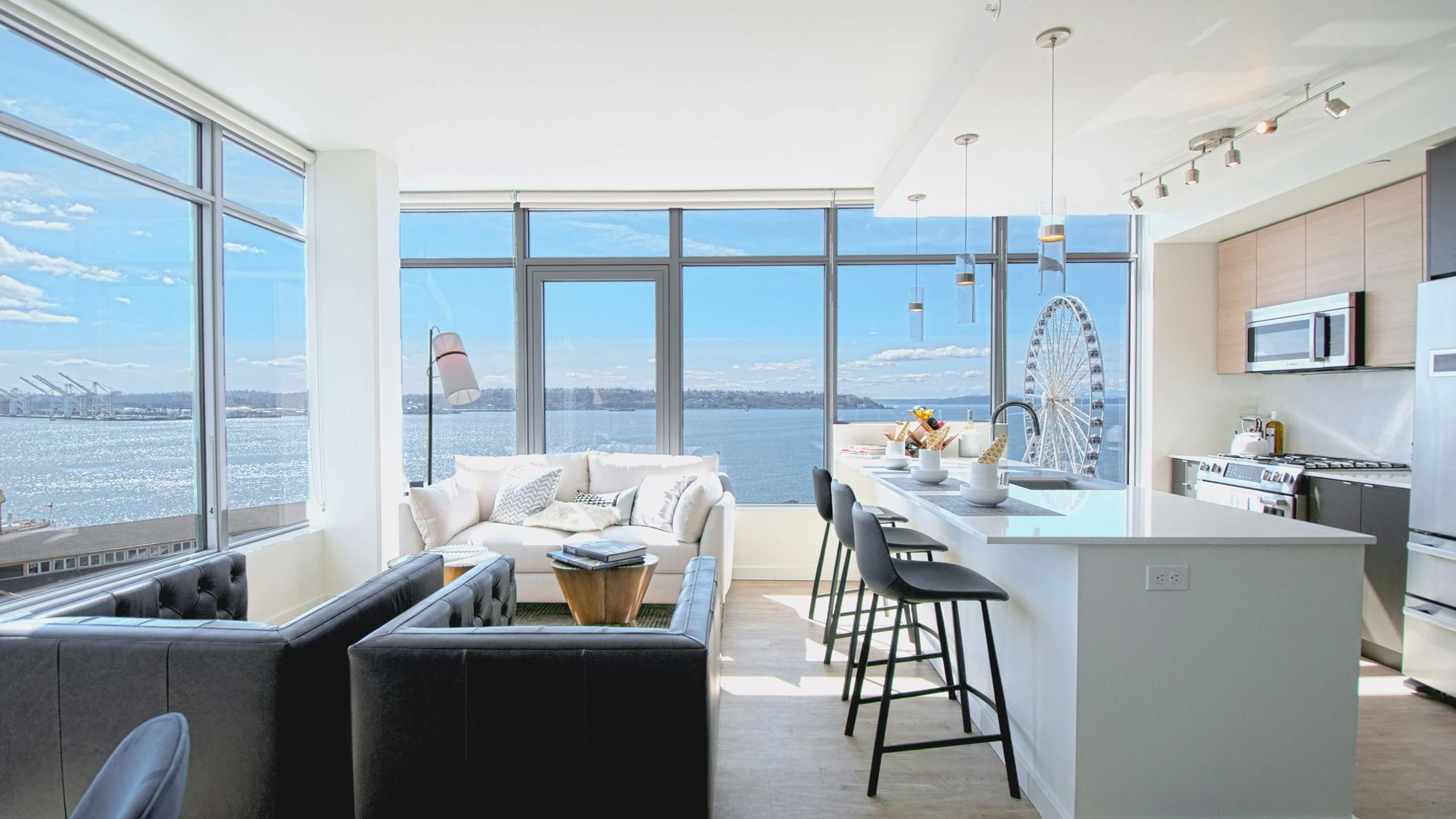 Corner living room at AMLI Waterfront apartments with white sofa, ferris wheel views, breakfast bar, and 2 walls of windows.