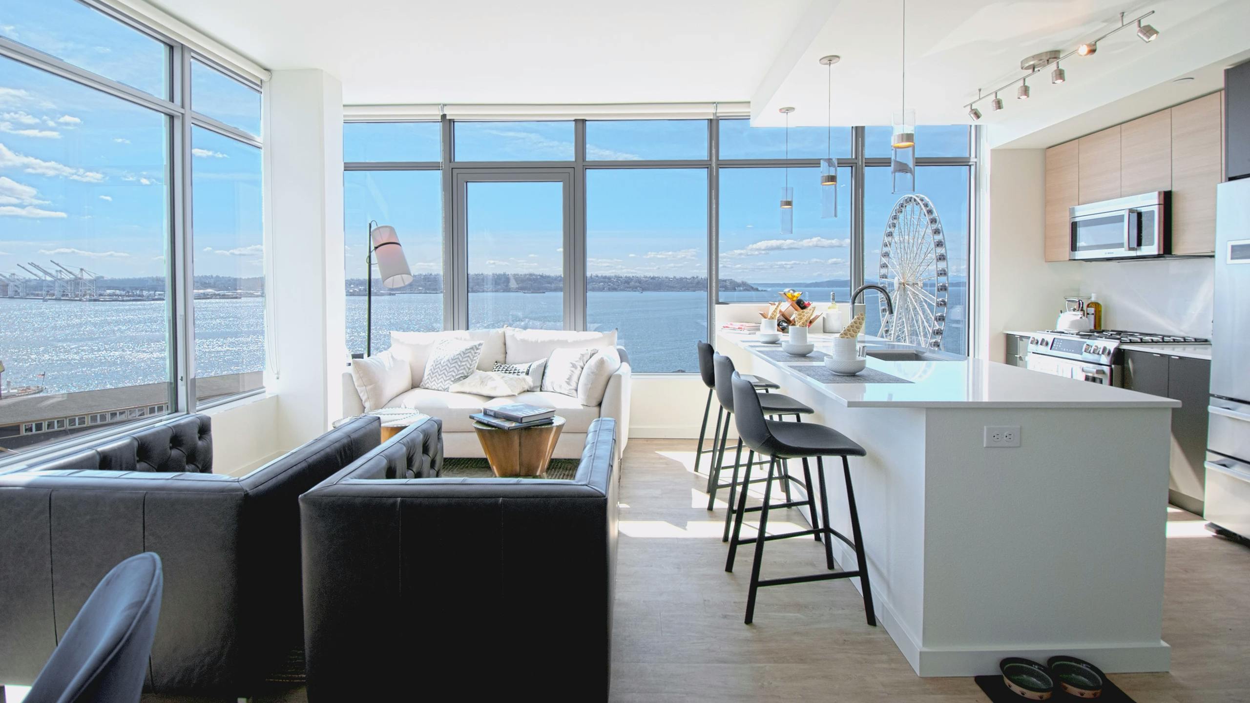 Corner living room at AMLI Waterfront apartments with white sofa, ferris wheel views, breakfast bar, and 2 walls of windows.