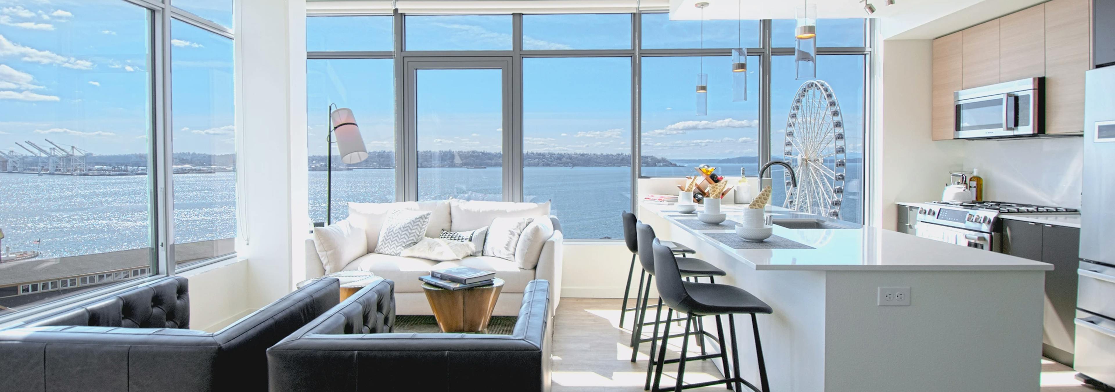 Corner living room at AMLI Waterfront apartments with white sofa, ferris wheel views, breakfast bar, and 2 walls of windows.