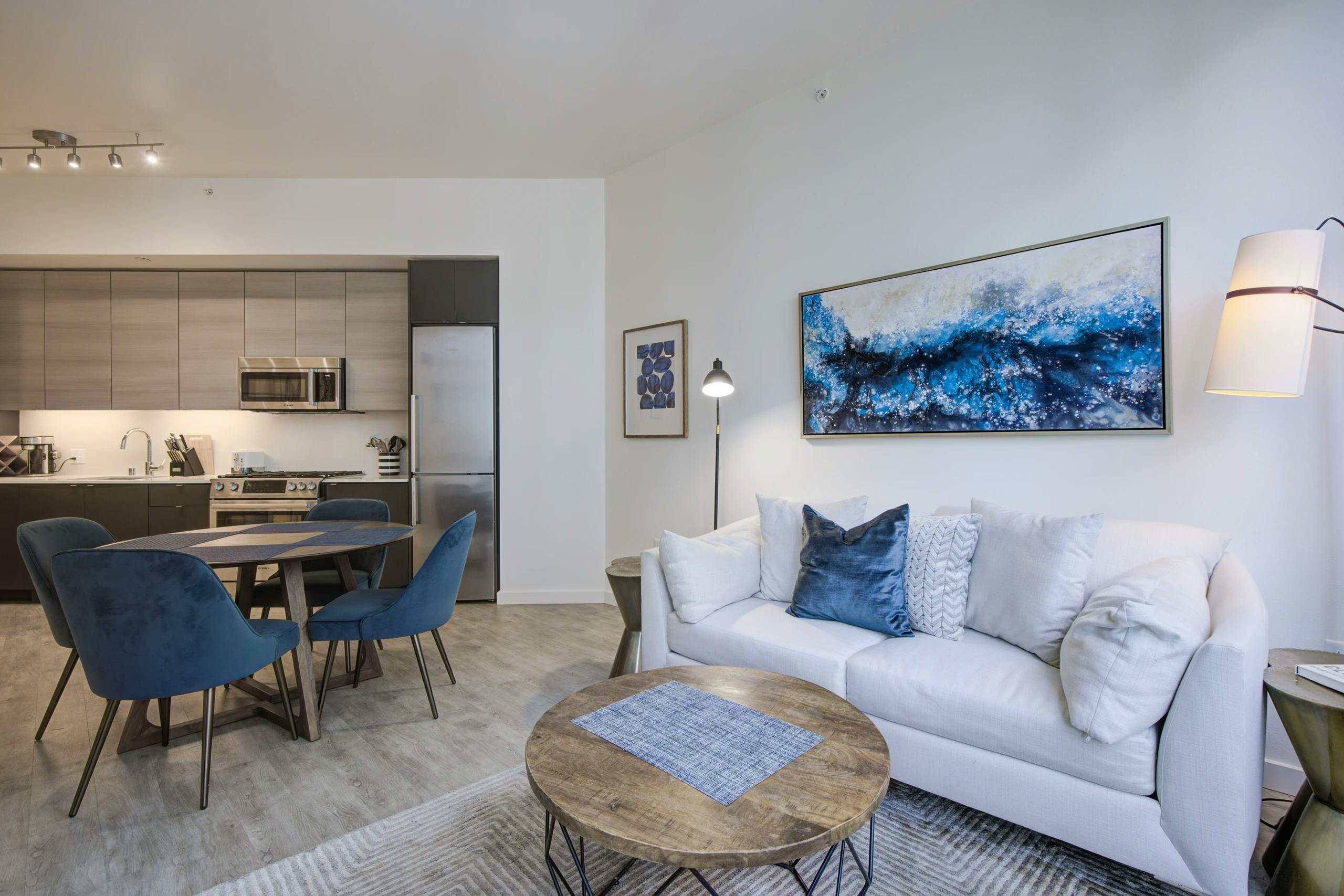 Living room and kitchen at AMLI Waterfront apartments with white sofa, blue chairs, round wood table and light wood cabinets.
