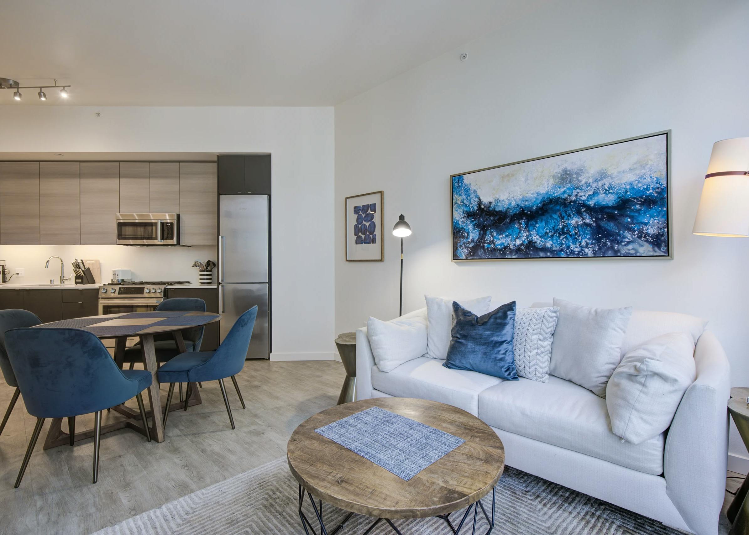 Living room and kitchen at AMLI Waterfront apartments with white sofa, blue chairs, round wood table and light wood cabinets.