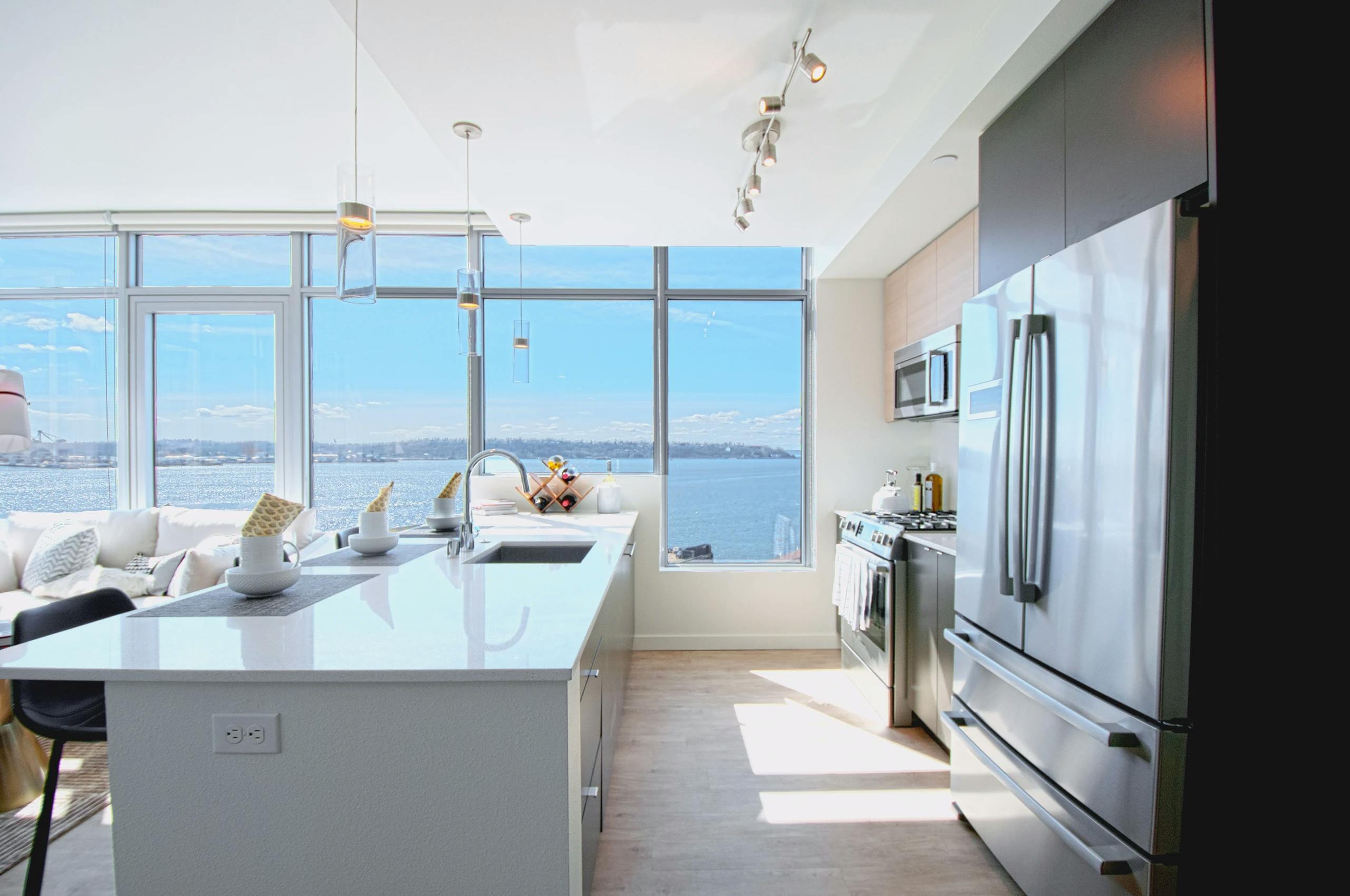 Waterfront facing kitchen with white quartz island, stainless steel refrigerator and full-height windows at AMLI Waterfront apartments.