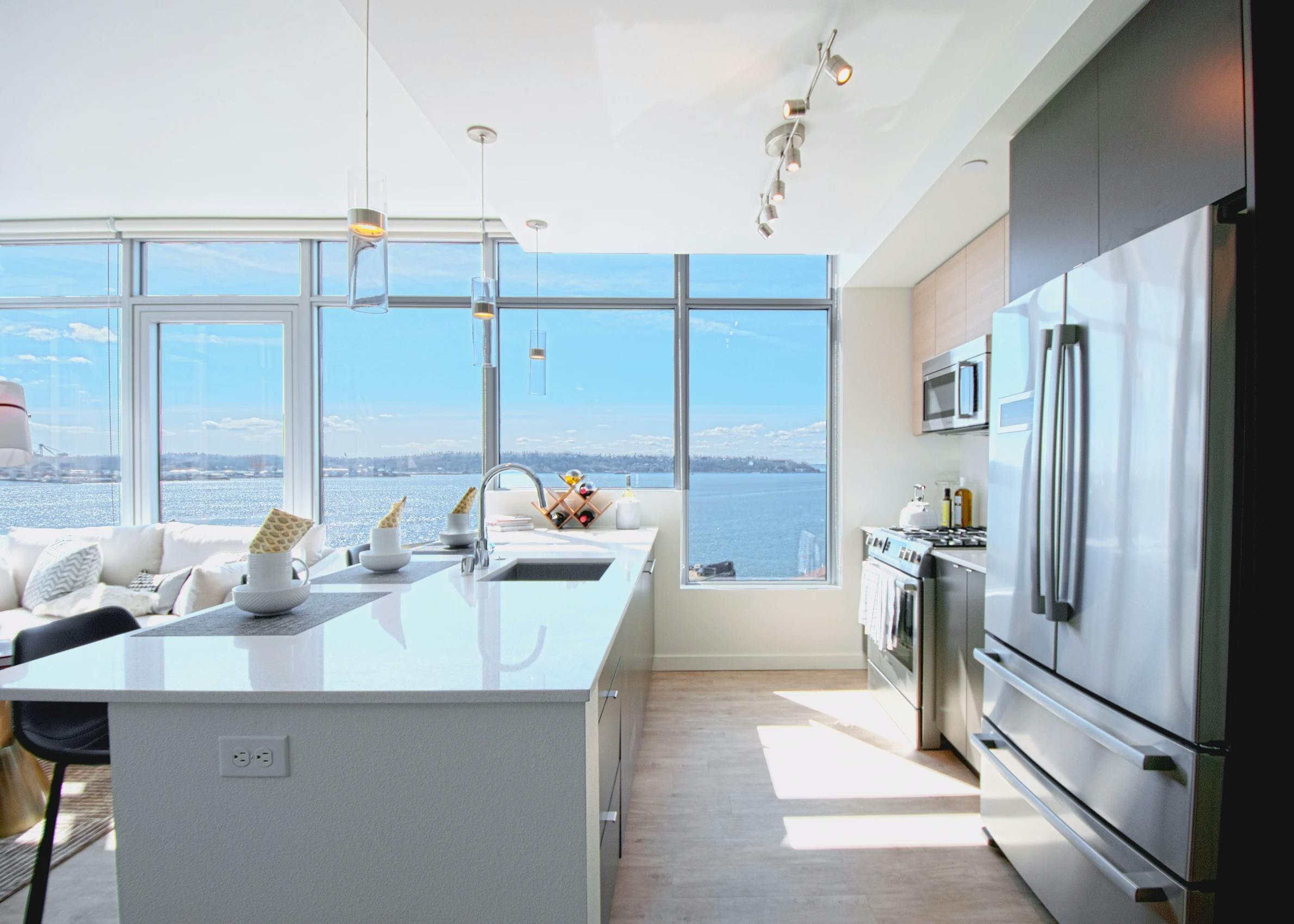 Waterfront facing kitchen with white quartz island, stainless steel refrigerator and full-height windows at AMLI Waterfront apartments.