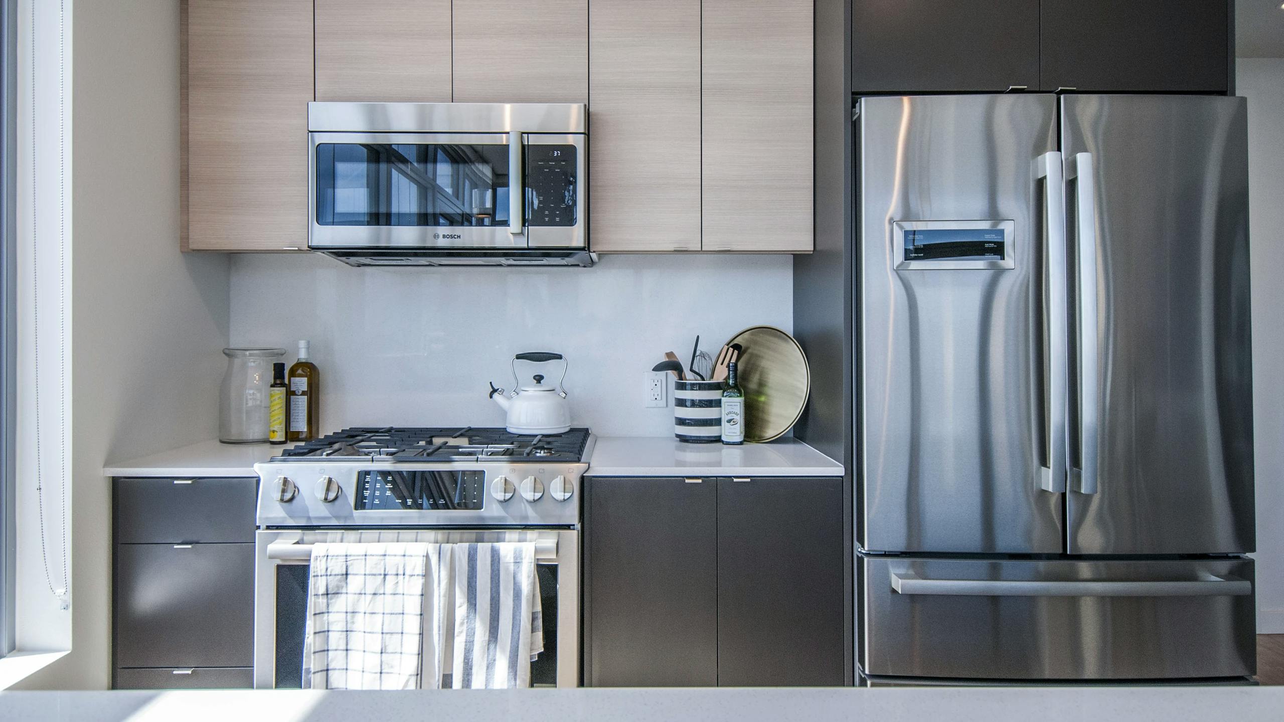 AMLI Waterfront apartment kitchen with stainless steel appliances, wood cabinets, gas range, and white quartz countertop.