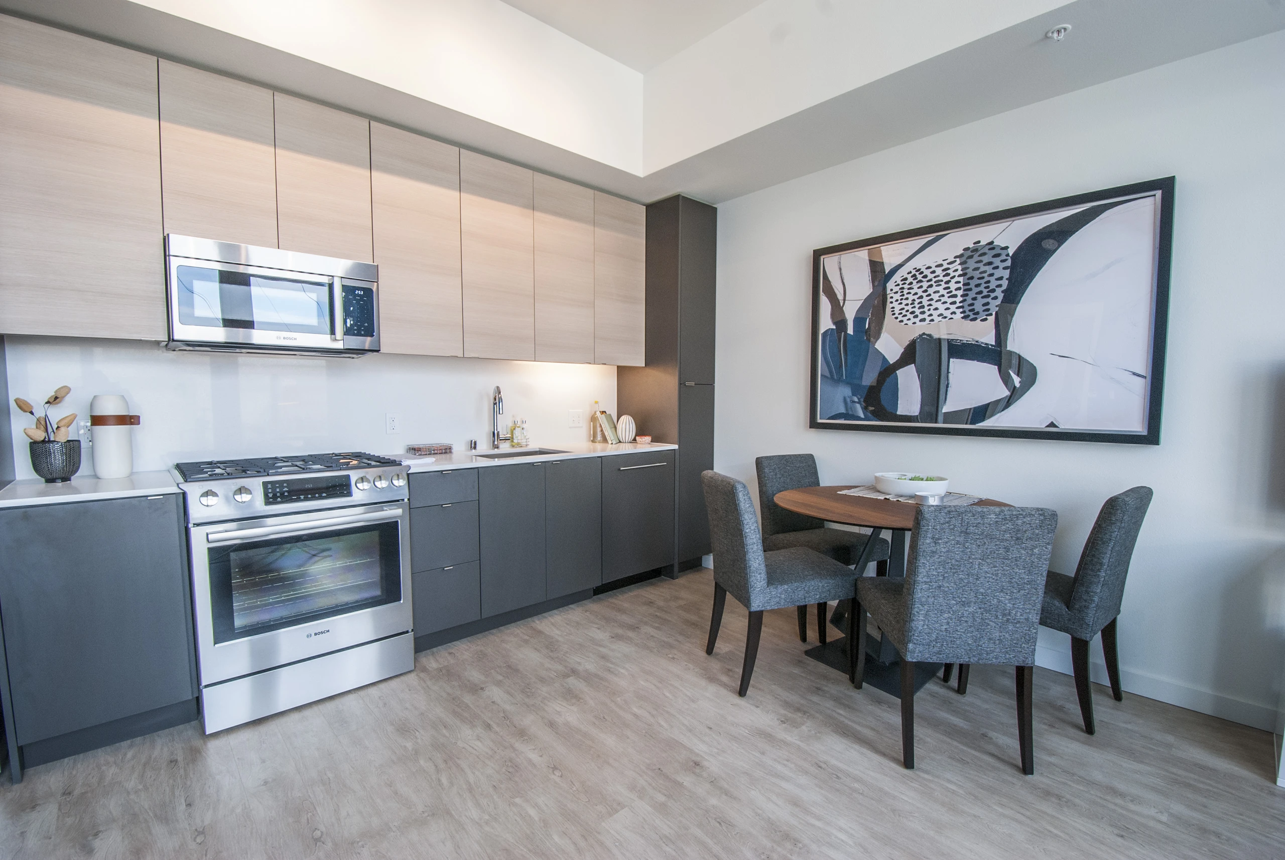 Kitchen and dining area at AMLI Waterfront apartments with light wood floors, stainless appliances, and round table with gray chairs.