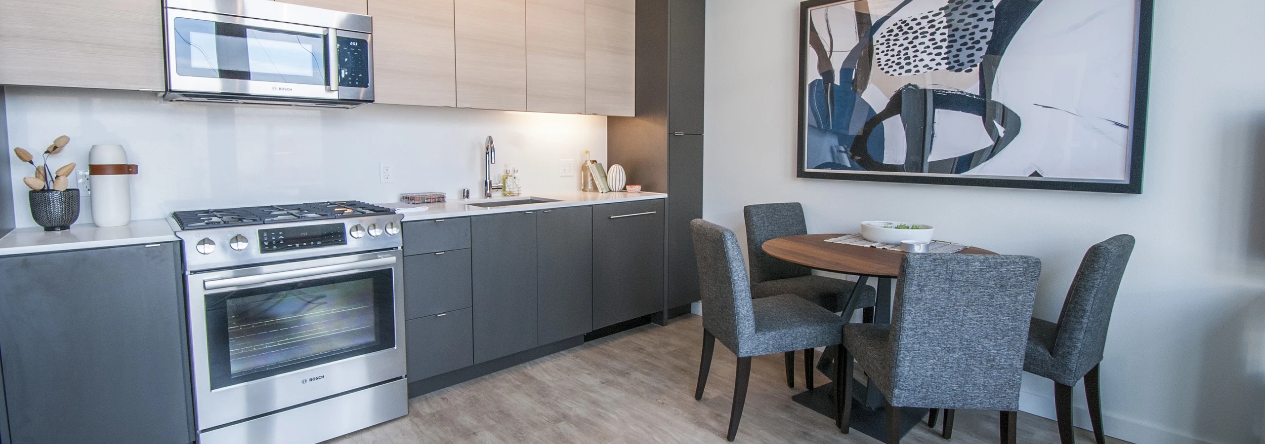 Kitchen and dining area at AMLI Waterfront apartments with light wood floors, stainless appliances, and round table with gray chairs.