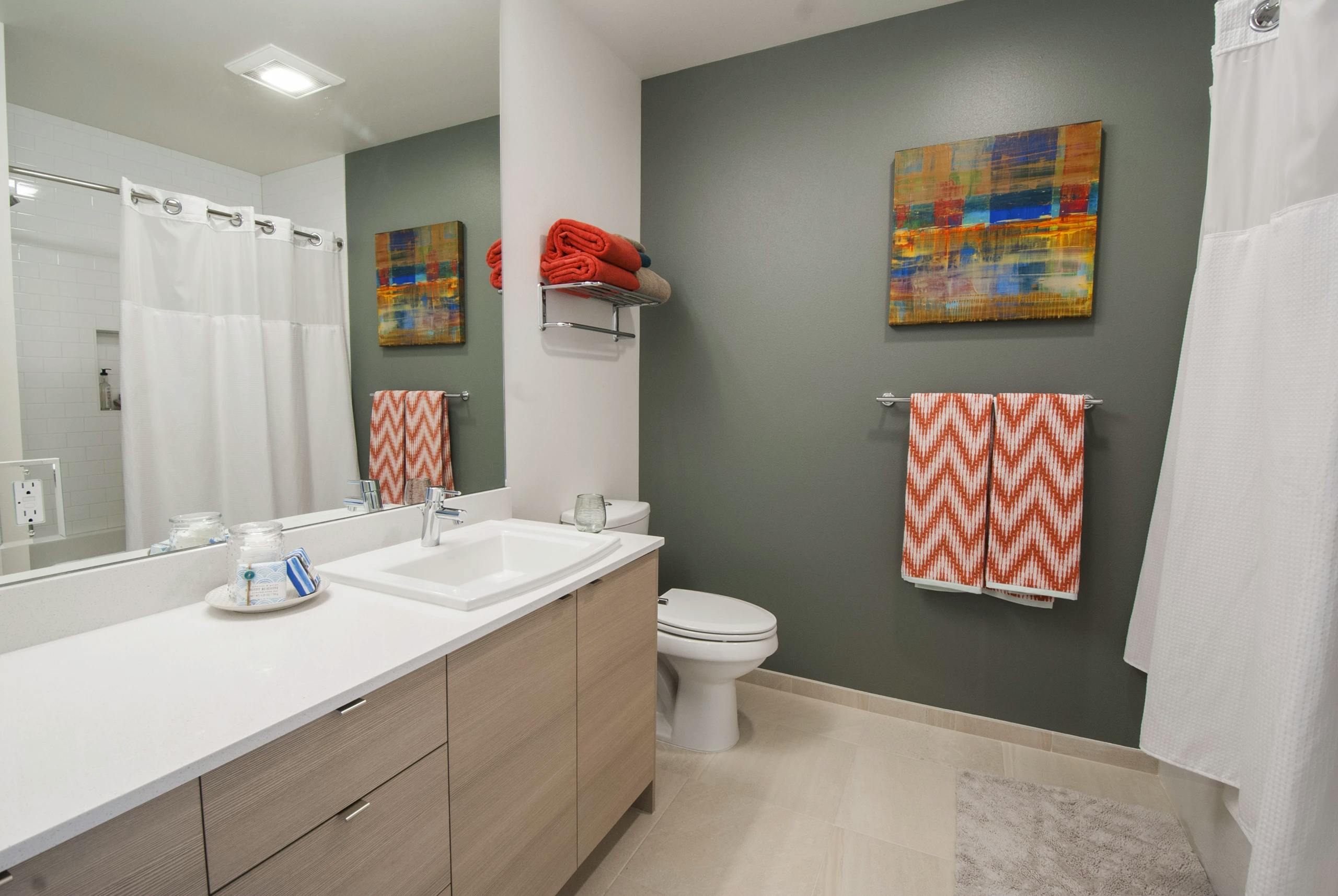 Bathroom with gray green accent wall, white shower curtain, and light wood vanity at AMLI Waterfront apartments.