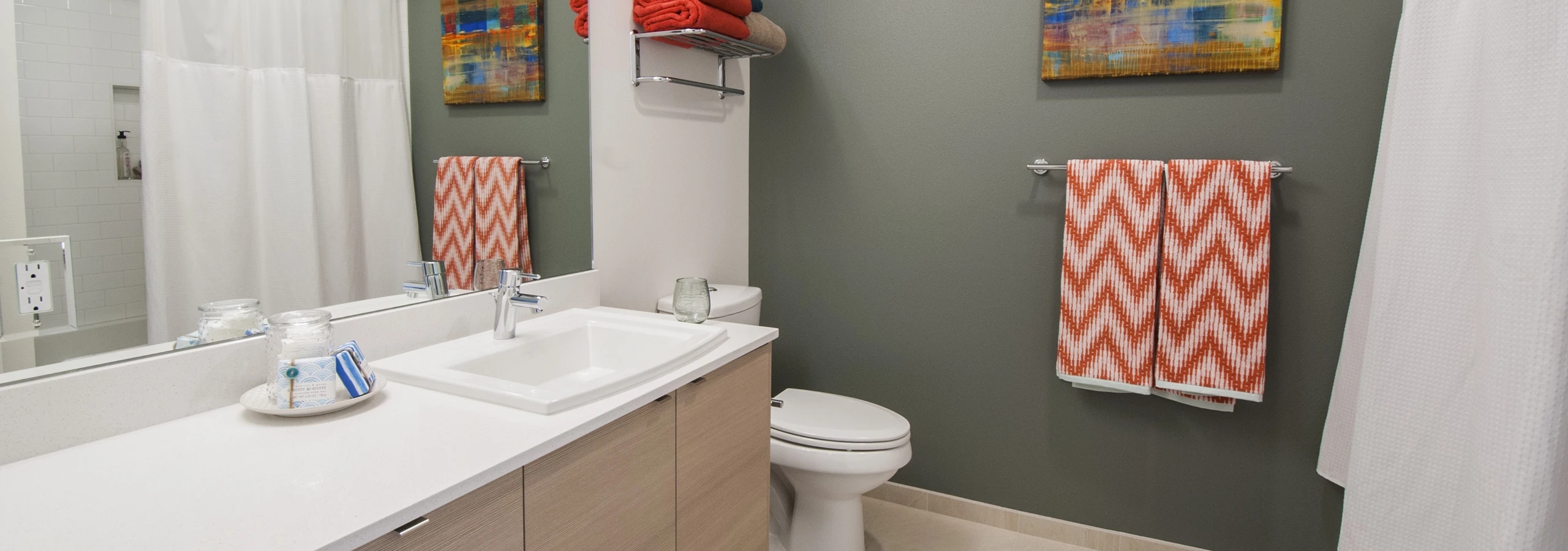 Bathroom with gray green accent wall, white shower curtain, and light wood vanity at AMLI Waterfront apartments.