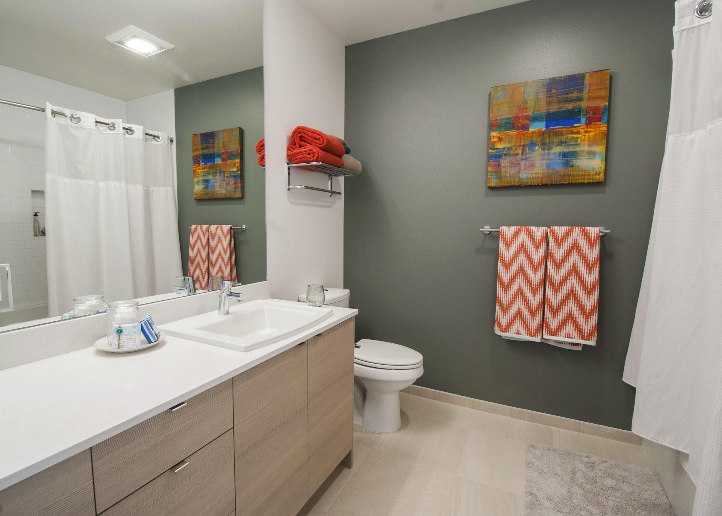 Bathroom with gray green accent wall, white shower curtain, and light wood vanity at AMLI Waterfront apartments.