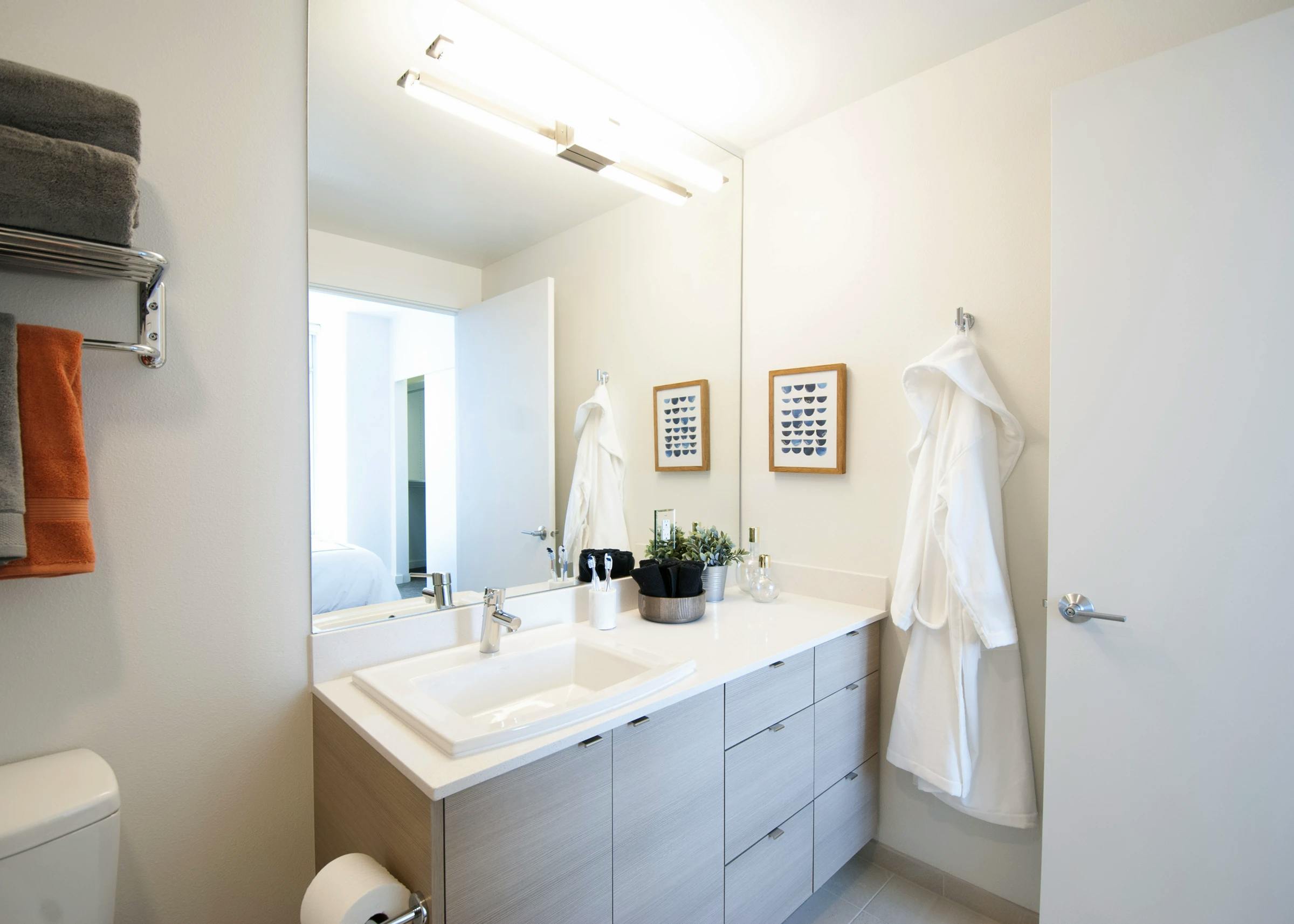 AMLI Waterfront apartment bathroom with light wood cabinetry, wall mirror, robe hook, and contemporary lighting.