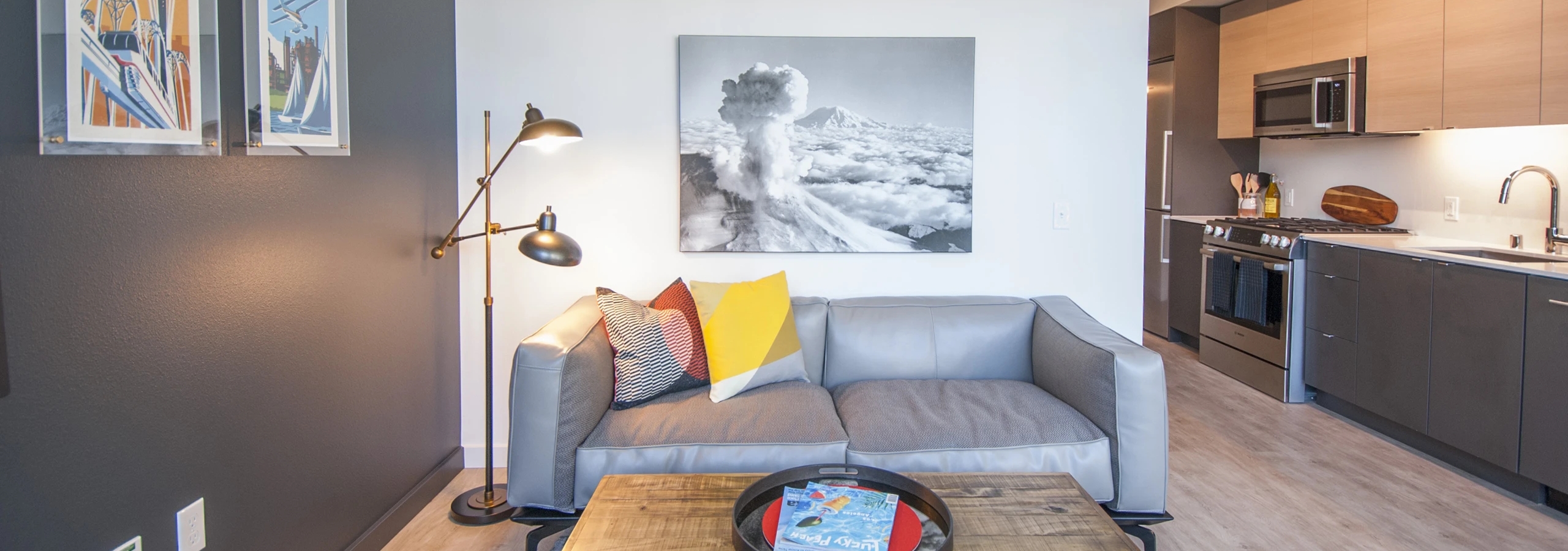 Interior view of AMLI Waterfront apartments with gray sofa, wood coffee table and kitchen with flat-panel cabinets.