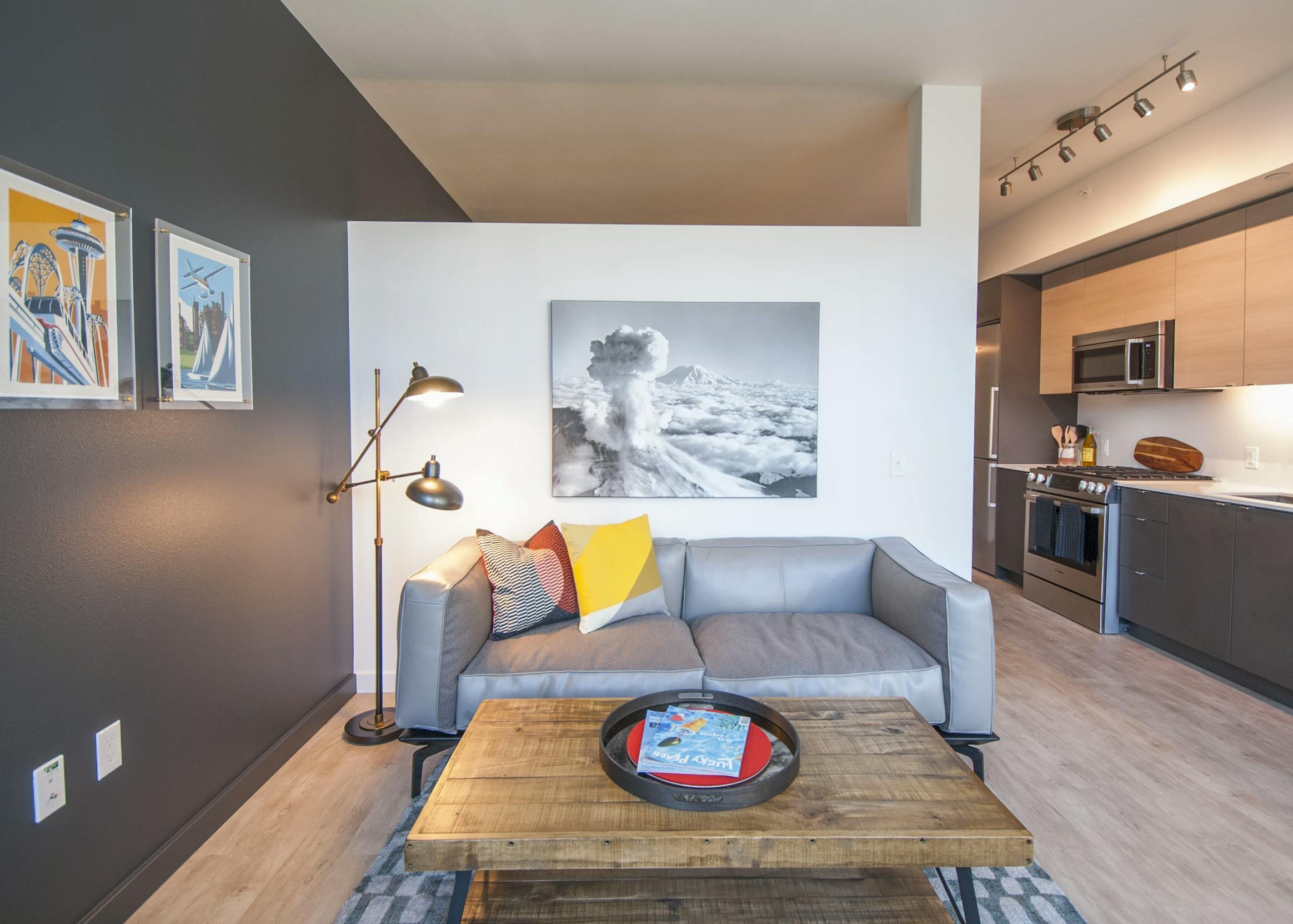 Interior view of AMLI Waterfront apartments with gray sofa, wood coffee table and kitchen with flat-panel cabinets.