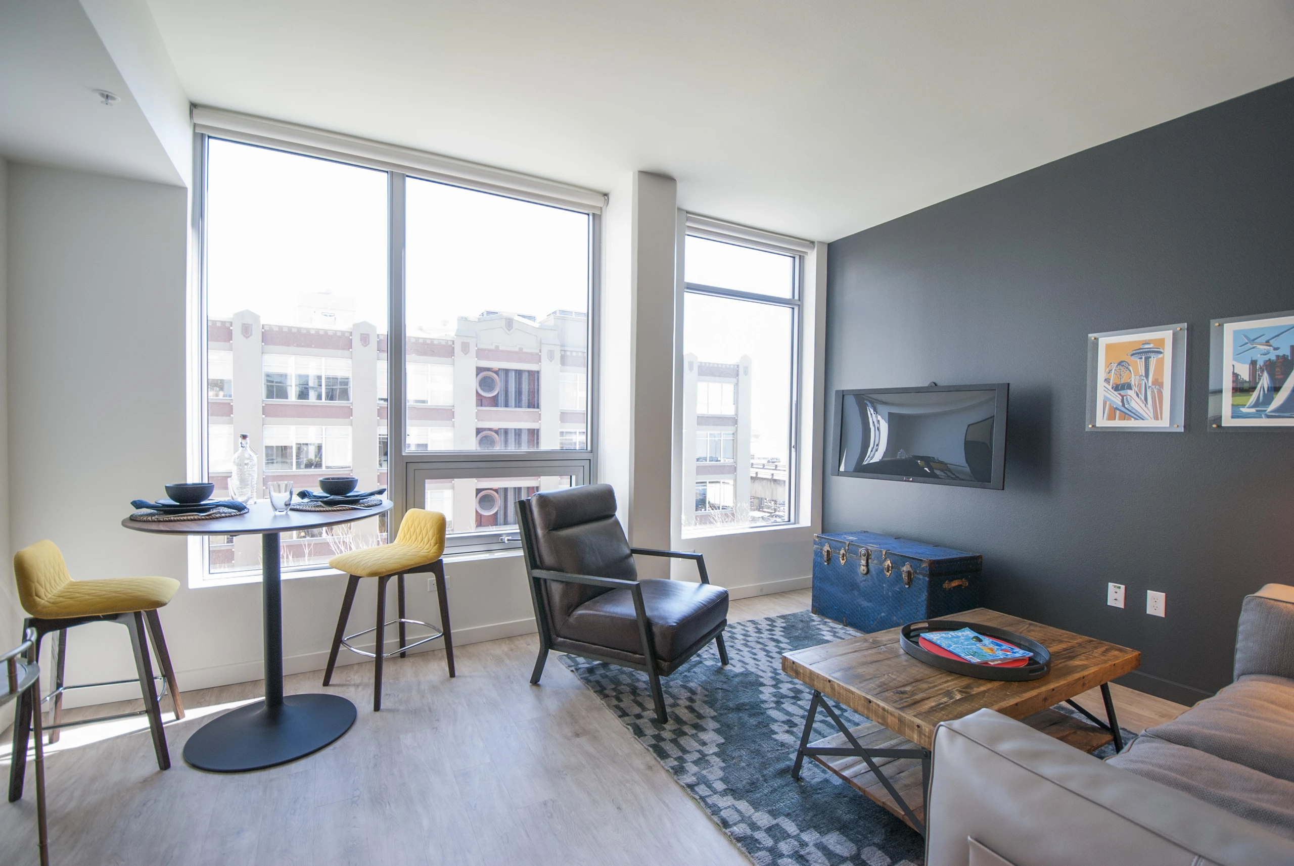 Living space at AMLI Waterfront apartments with leather armchair, yellow barstools at high top table, and oversized windows.