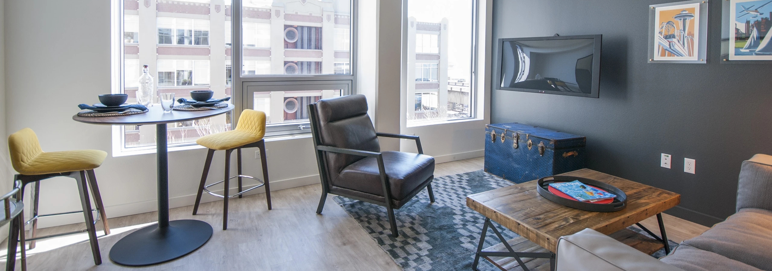 Living space at AMLI Waterfront apartments with leather armchair, yellow barstools at high top table, and oversized windows.