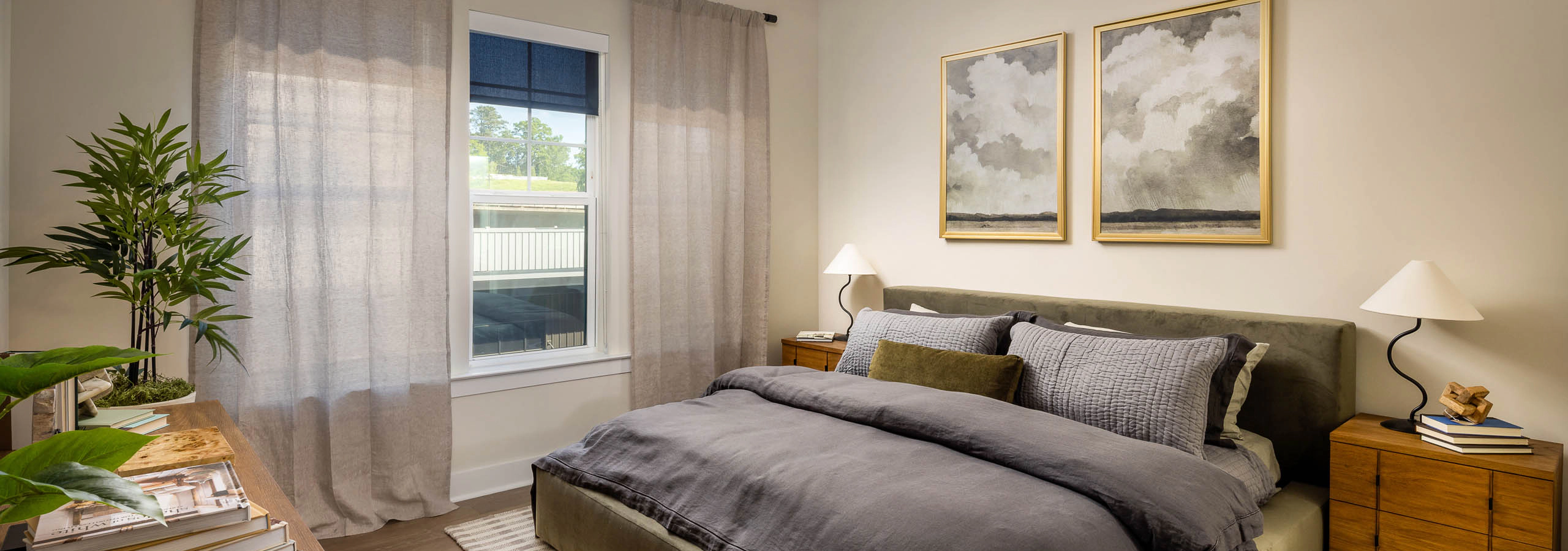 Bedroom at AMLI Brookhaven apartments with hardwood flooring and a ceiling fan and a bed with a grey comforter blanket and a window.