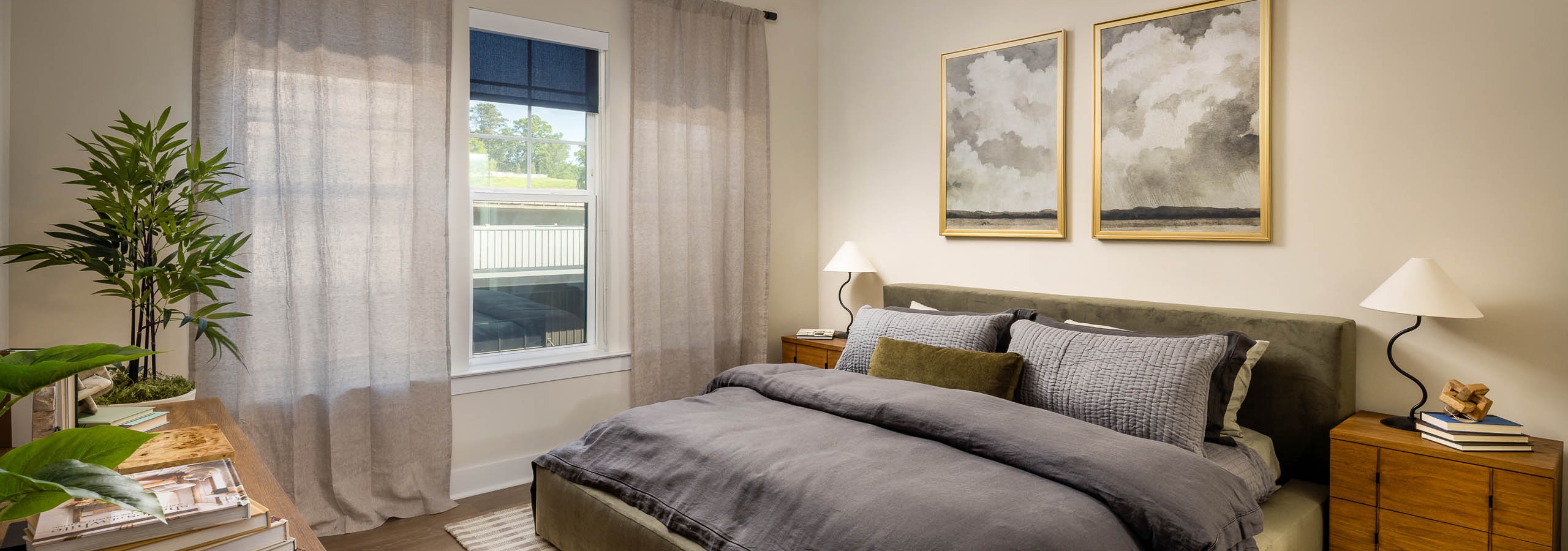 Bedroom at AMLI Brookhaven apartments with hardwood flooring and a ceiling fan and a bed with a grey comforter blanket and a window.