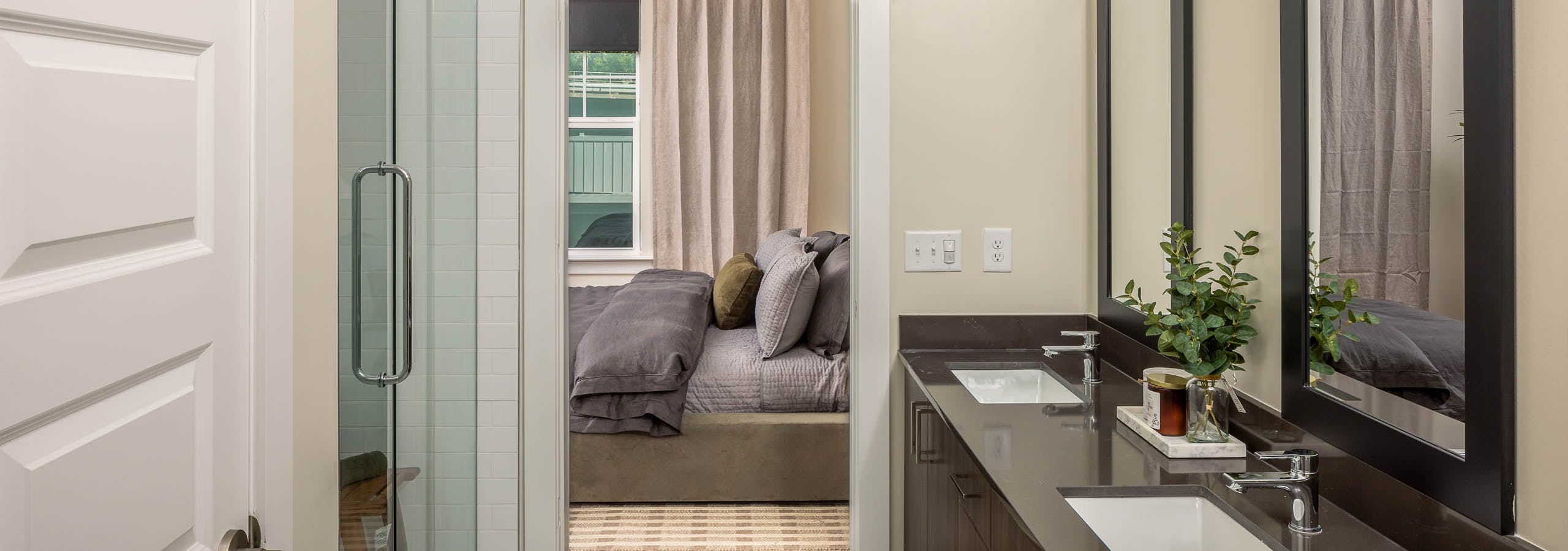 AMLI Brookhaven bathroom with two sinks and mirrors with black borders and a glass door shower with a view into the bedroom.
