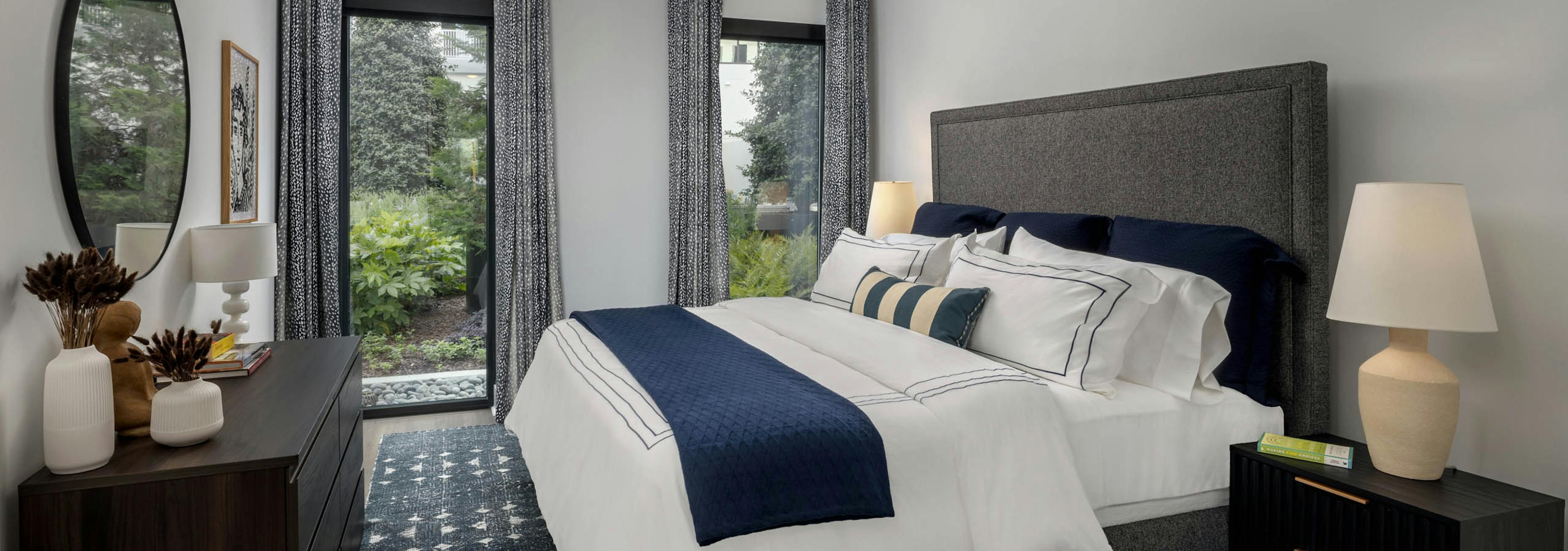AMLI Atlantic Station apartment bedroom with a king gray upholstered bed with white and navy bedding and curtained windows