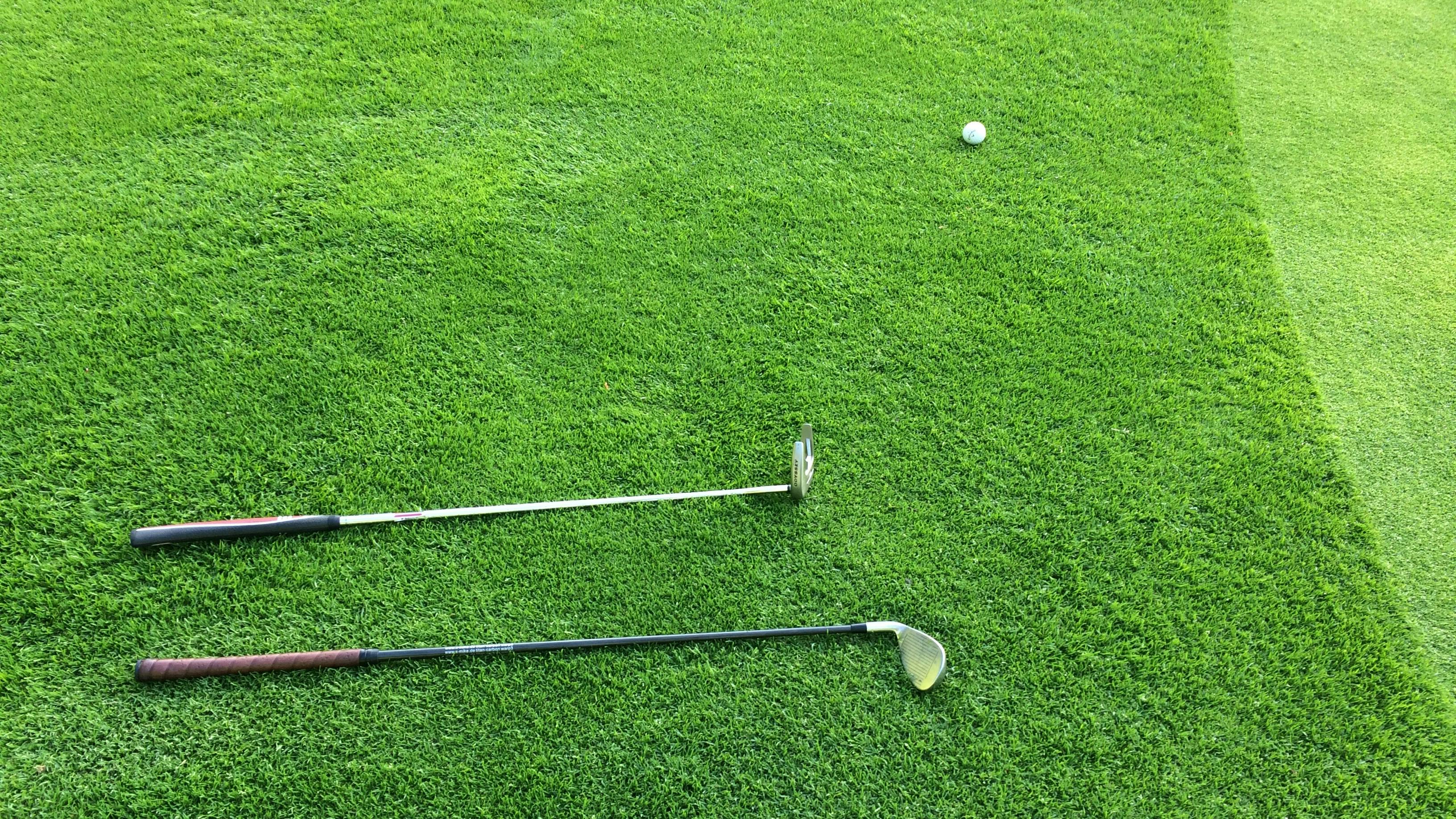 An overhead view of two golf clubs and a golf ball lying on a manicured green.