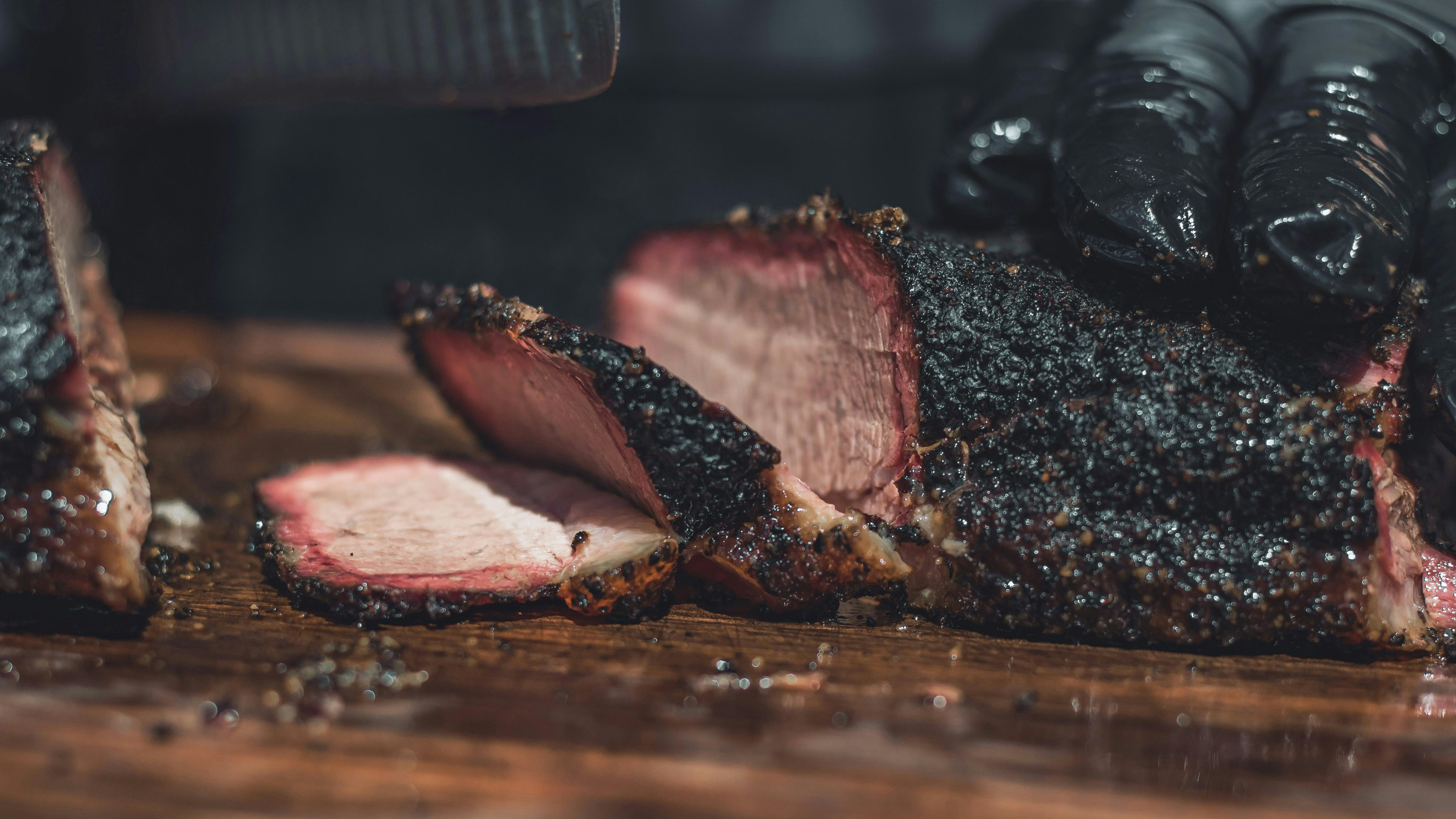 A close-up shot of a person's gloved hands slicing a large, well-crusted piece of smoked brisket on a wooden cutting board.