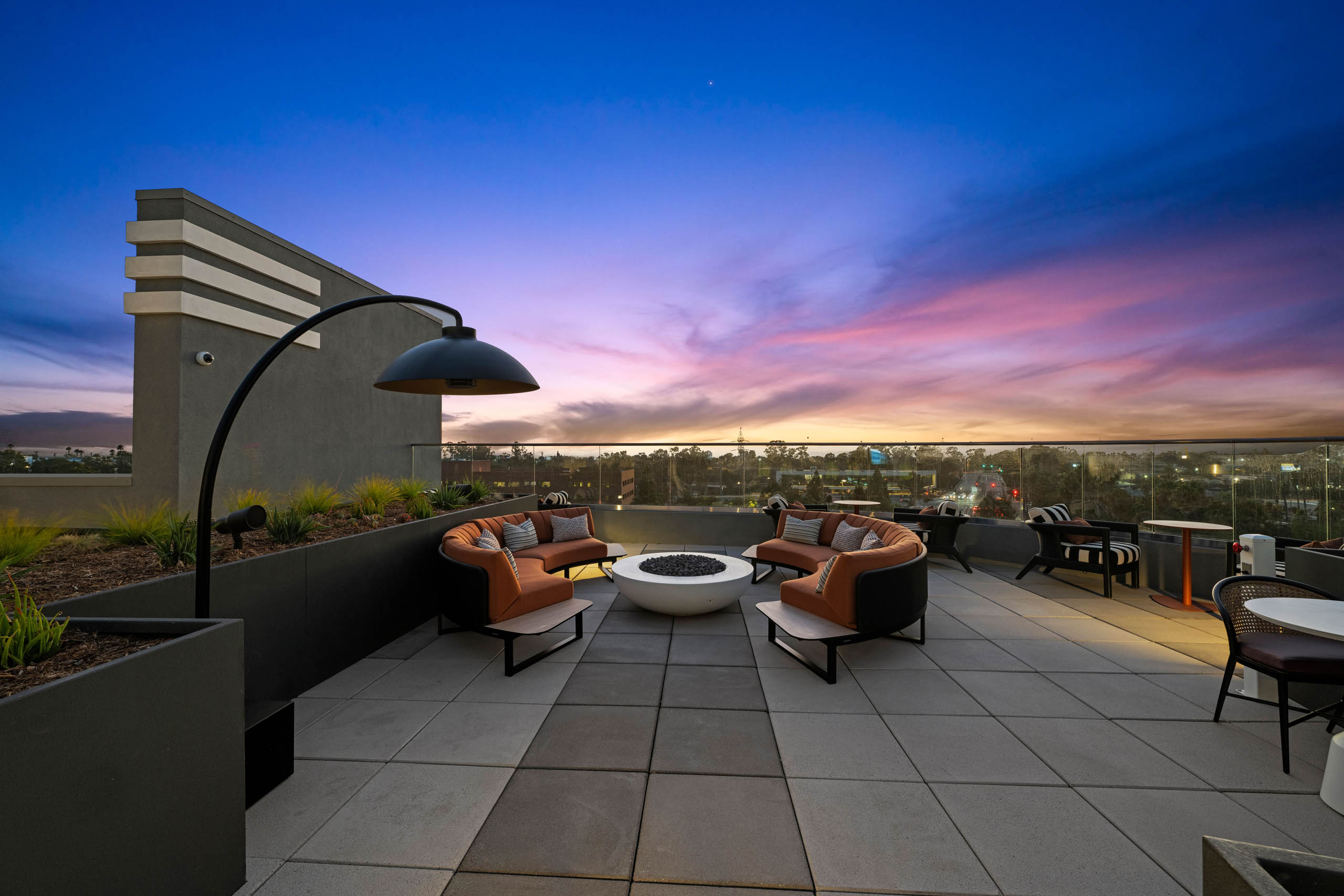 Rooftop fire pit seating at AMLI Aero apartments with modern arched couches, outdoor lighting, and sunset views over the city.