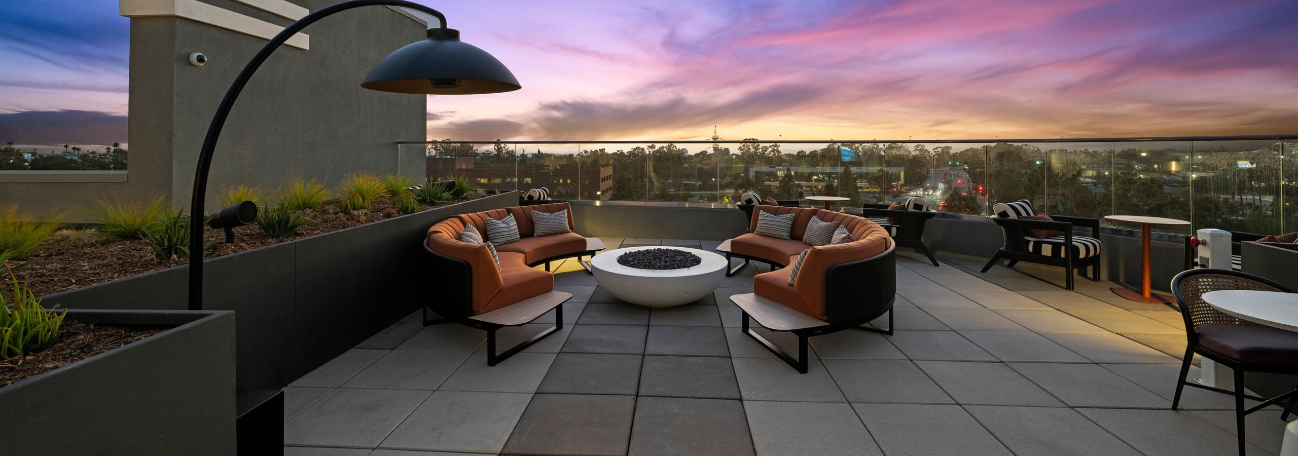 Rooftop fire pit seating at AMLI Aero apartments with modern arched couches, outdoor lighting, and sunset views over the city.