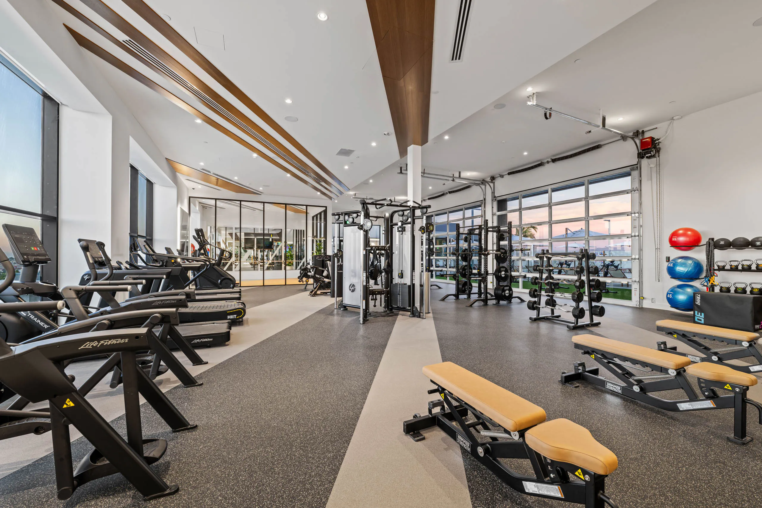 Fitness center at AMLI Aero apartments with treadmills, weight machines, benches, and floor-to-ceiling windows with bright lighting.