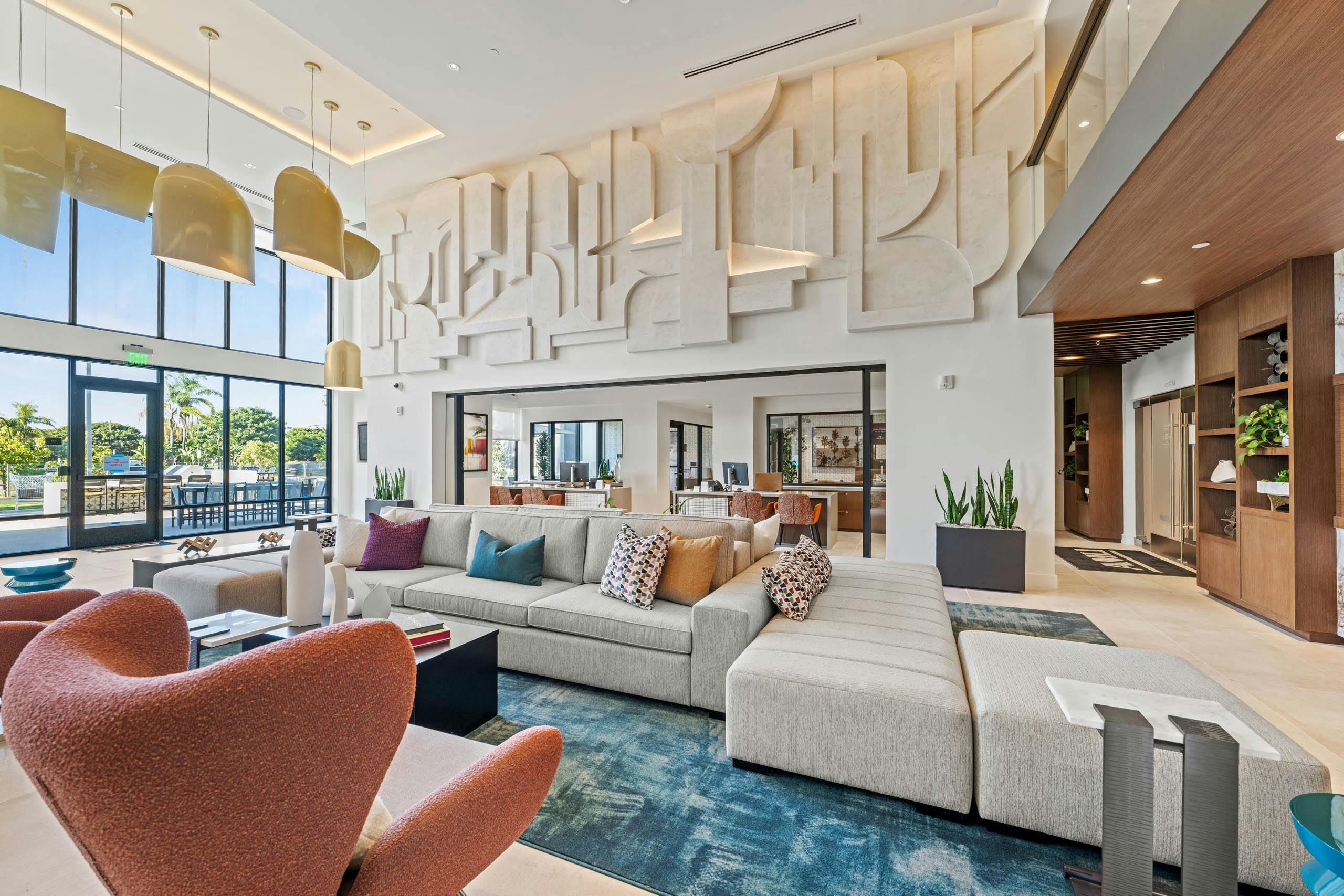 Lobby at AMLI Aero apartments with modern sectional, colorful pillows, bold accent chairs, tall windows and geometric wall design.