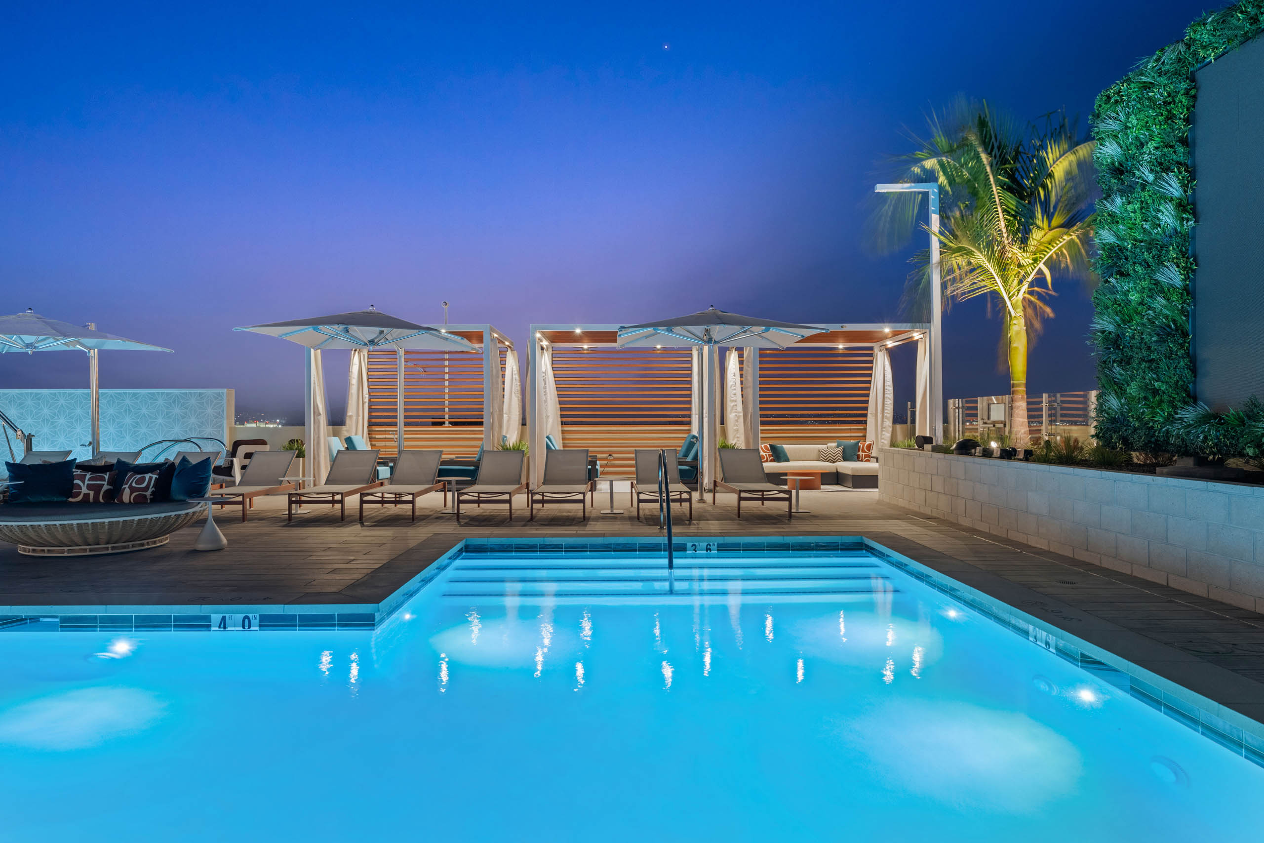Cabanas with wood slat accents at AMLI Aero apartments rooftop pool with lounge chairs, umbrellas, palm trees, and under evening sky.