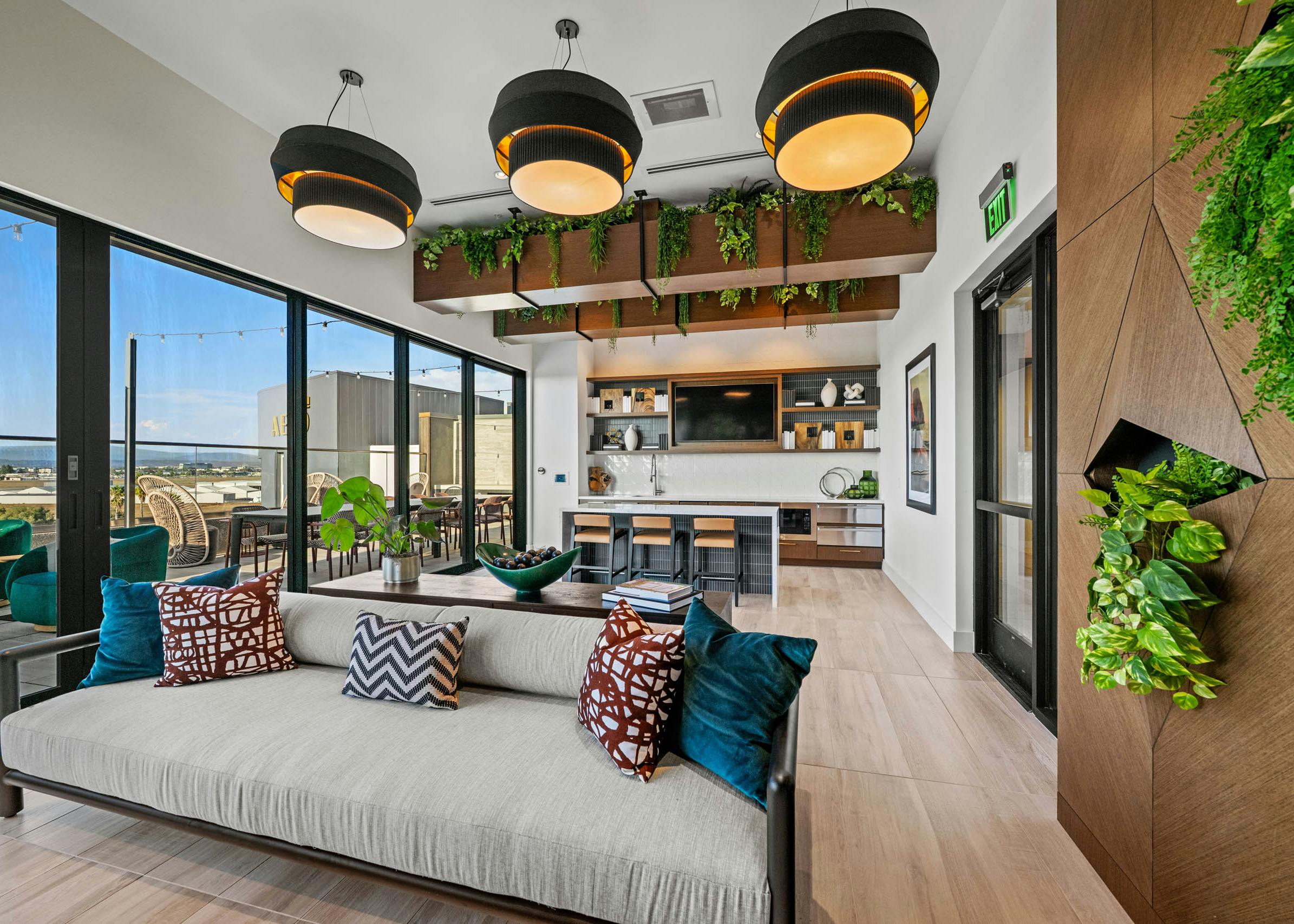 Interior daytime view of AMLI Aero apartments Sunset rooftop lounge with sofa, hanging lights, greenery, and kitchen with island seating.