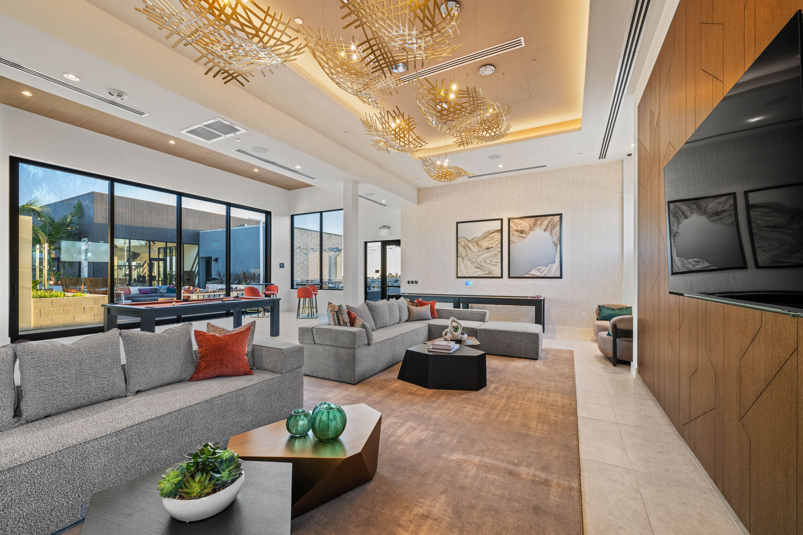 Clubroom at AMLI Aero apartments with gray sectionals, accent pillows, modern lighting, wall art, and large windows to terrace.
