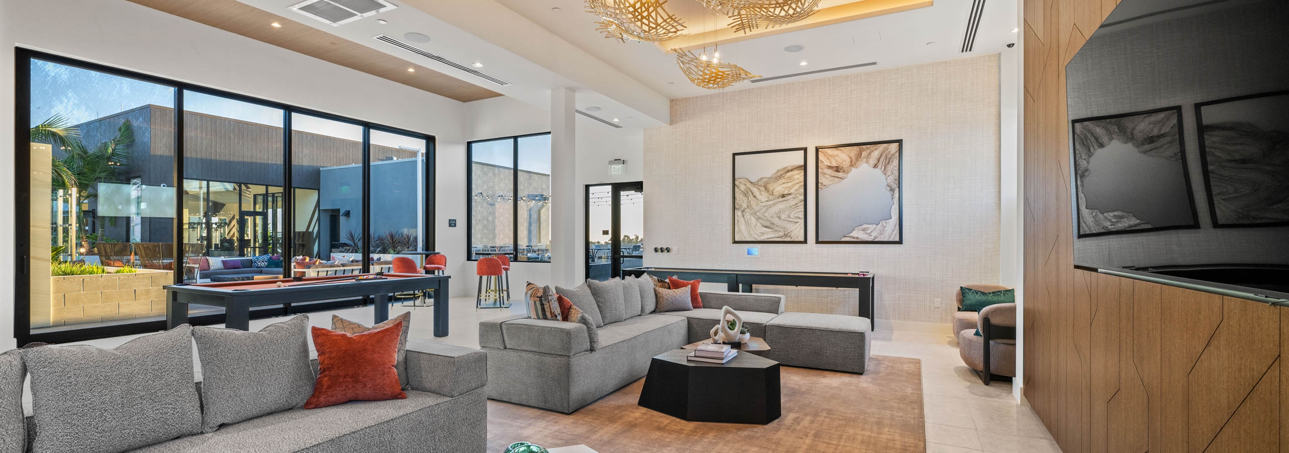 Clubroom at AMLI Aero apartments with gray sectionals, accent pillows, modern lighting, wall art, and large windows to terrace.