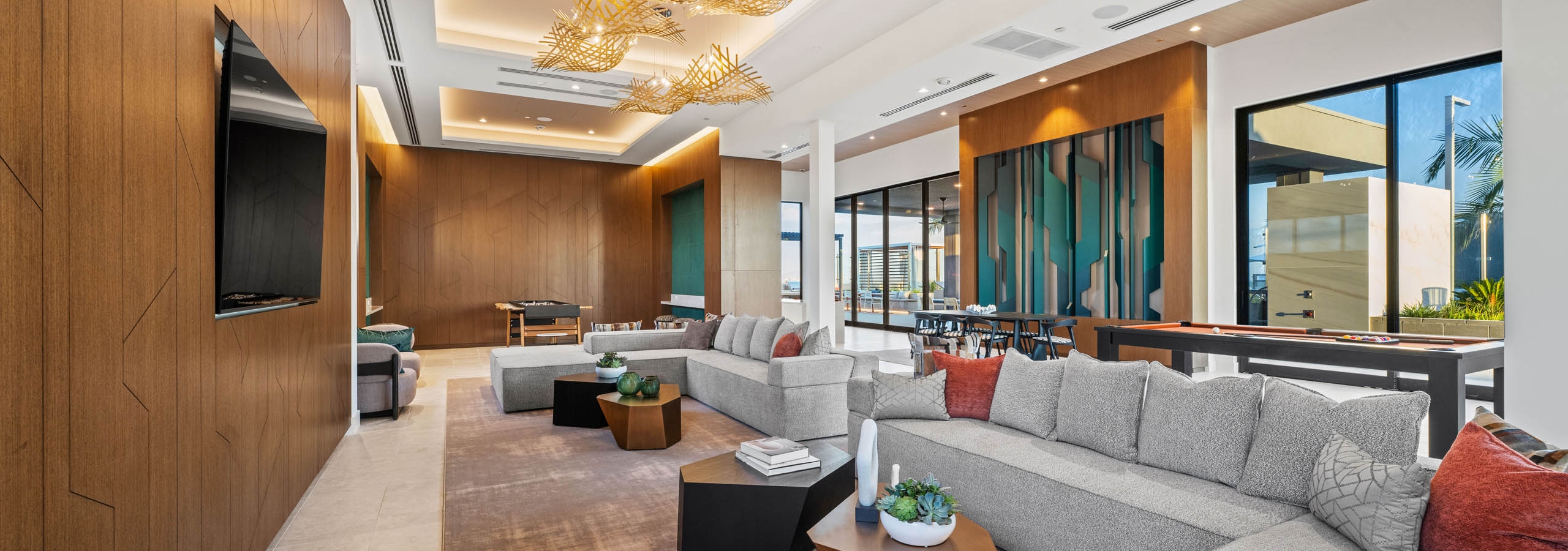 Clubroom with sectional gray sofas, modern lighting, wood accent walls, and large windows opening to terrace at AMLI Aero apartments.