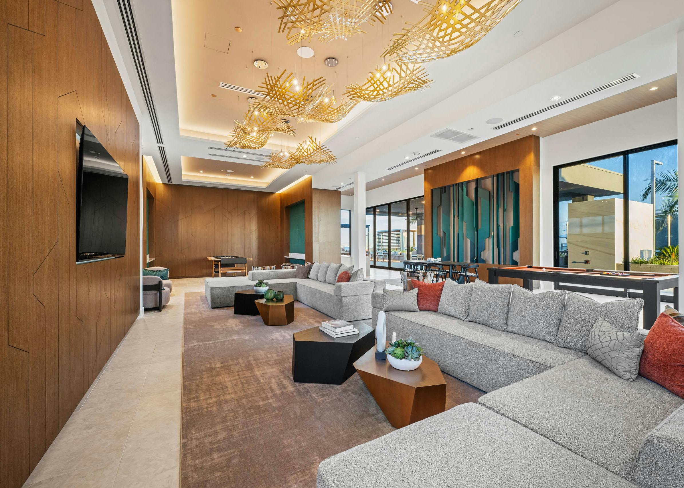 Clubroom with sectional gray sofas, modern lighting, wood accent walls, and large windows opening to terrace at AMLI Aero apartments.