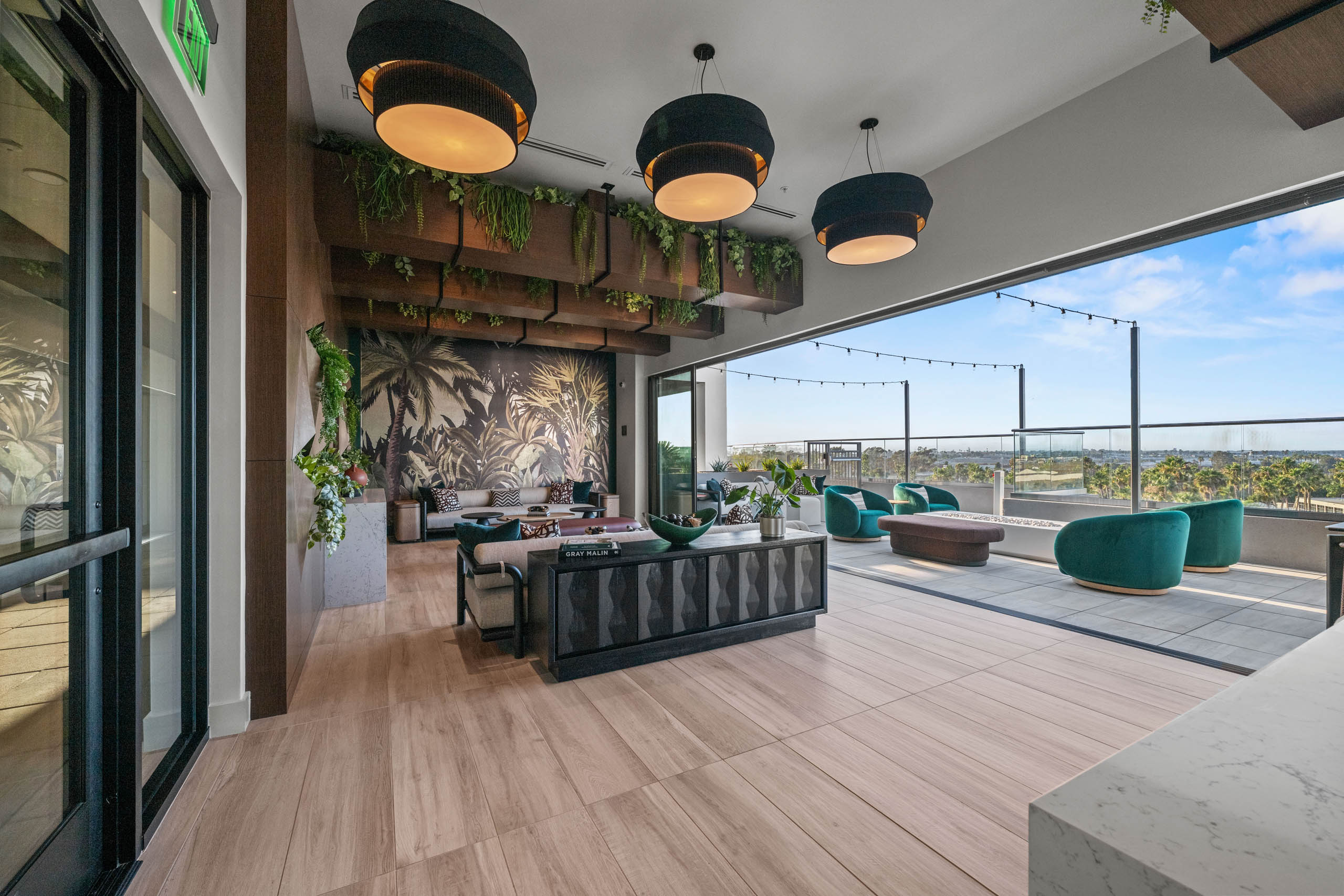 Indoor and outdoor connected jungle themed room at AMLI Aero with wood flooring and luxurious sofa and fabrics with string lights.