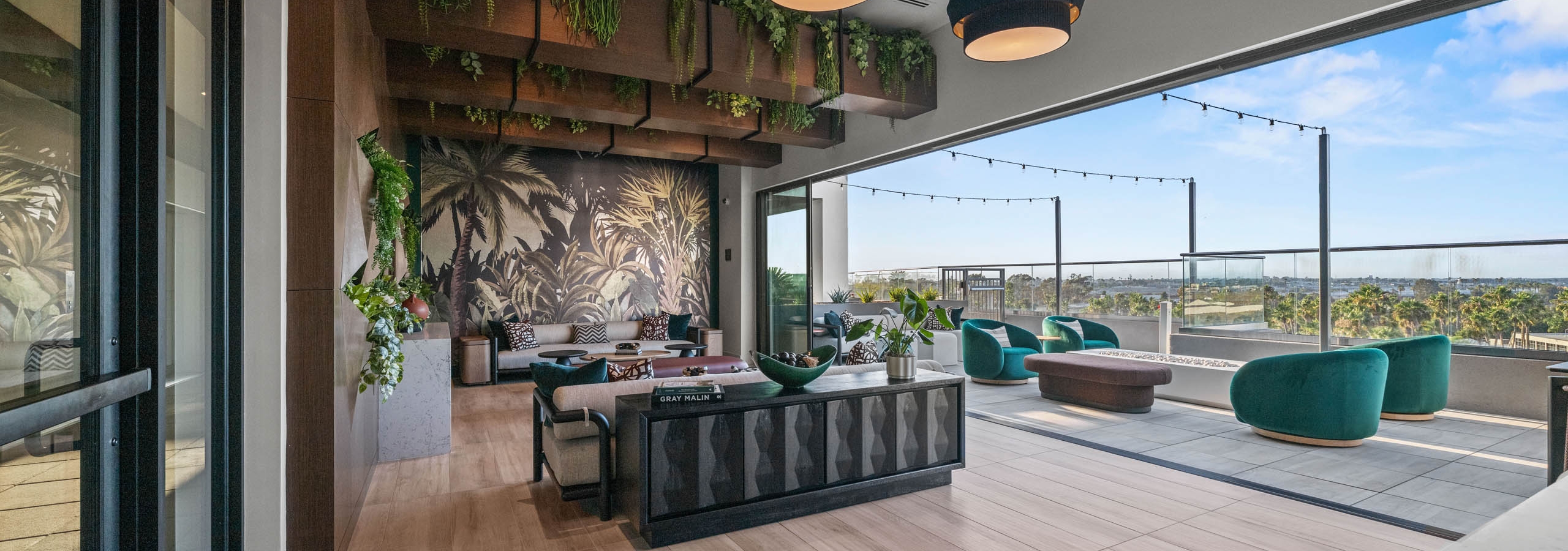 Indoor and outdoor connected jungle themed room at AMLI Aero with wood flooring and luxurious sofa and fabrics with string lights.