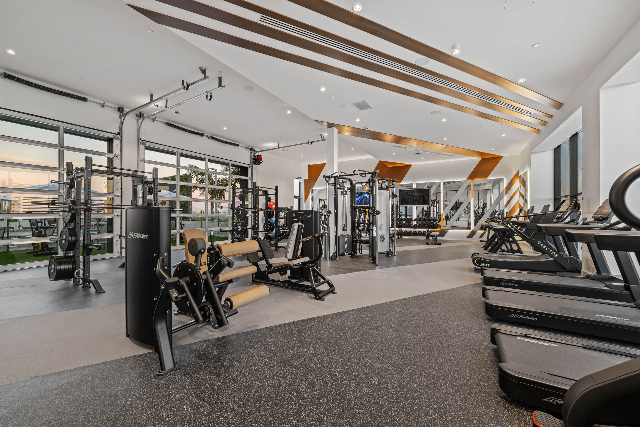 Fitness center at AMLI Aero apartments with treadmills, weight machines, benches, and floor-to-ceiling windows with bright lighting.