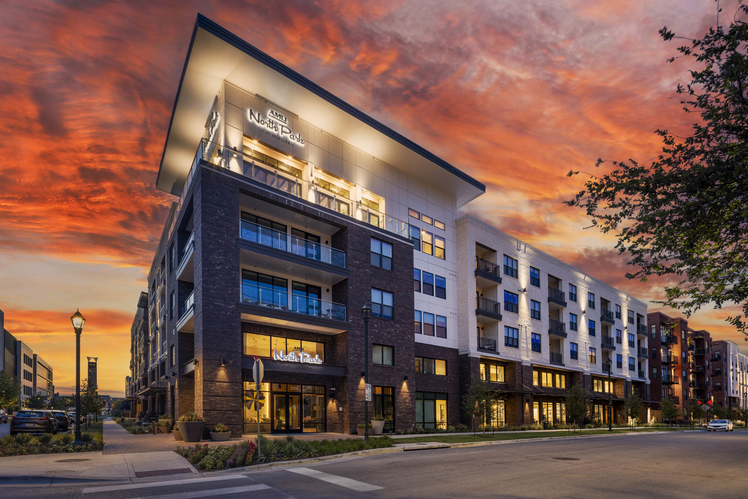 Sunset view of AMLI North Park apartment building with brick and light facade balconies retail spaces streetlights and trees