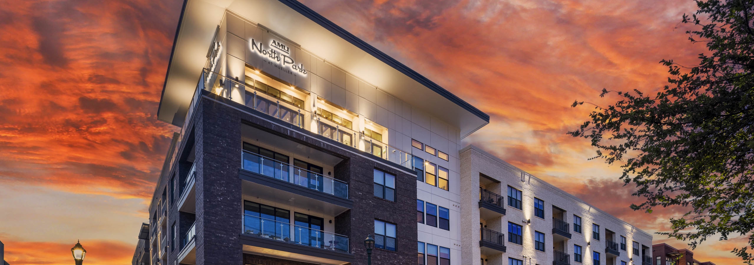 Sunset view of AMLI North Park apartment building with brick and light facade balconies retail spaces streetlights and trees