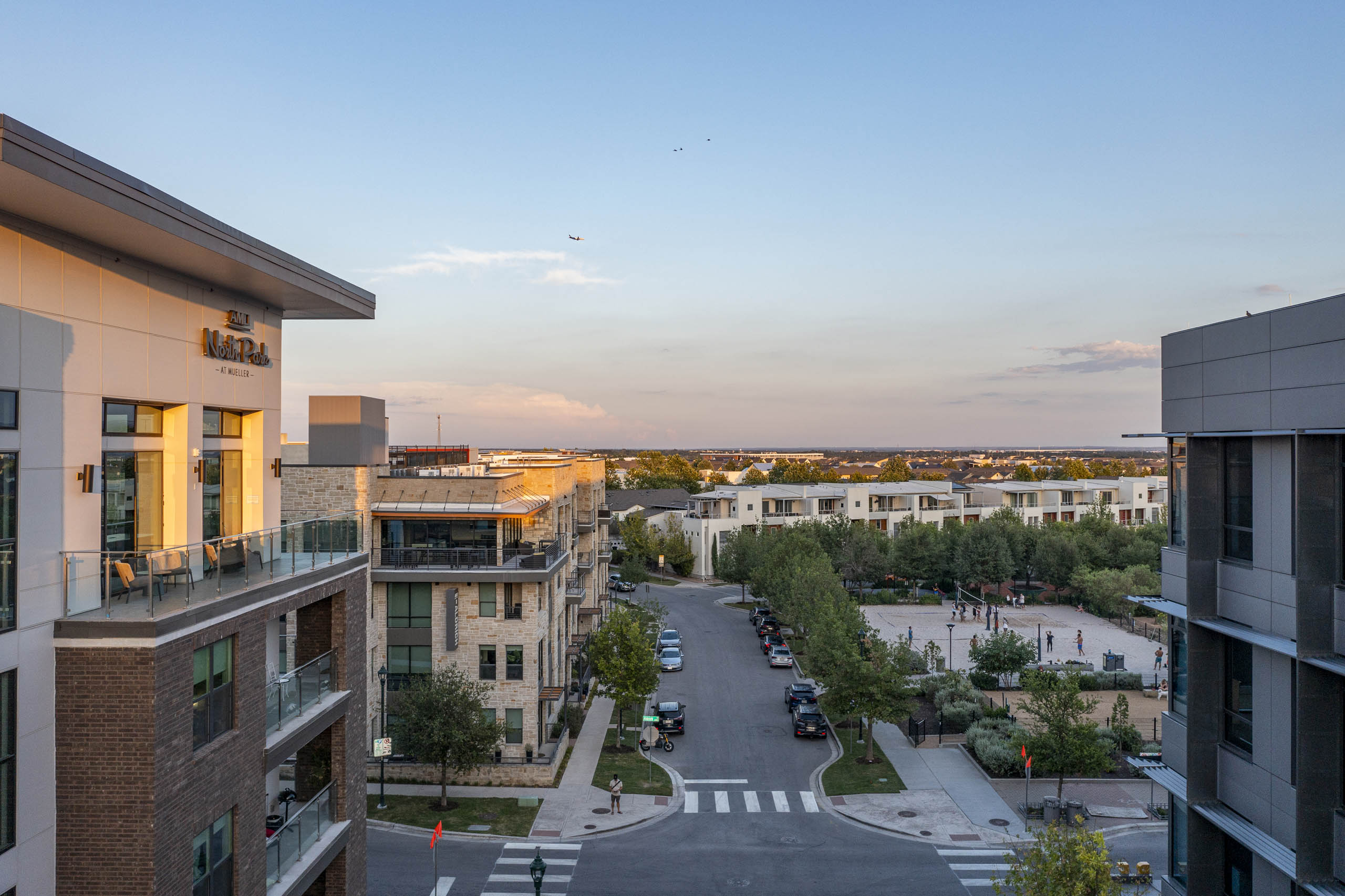 Sunset view of AMLI North Park apartment building kitty corner from park with beach volleyball court and tree lined sidewalks