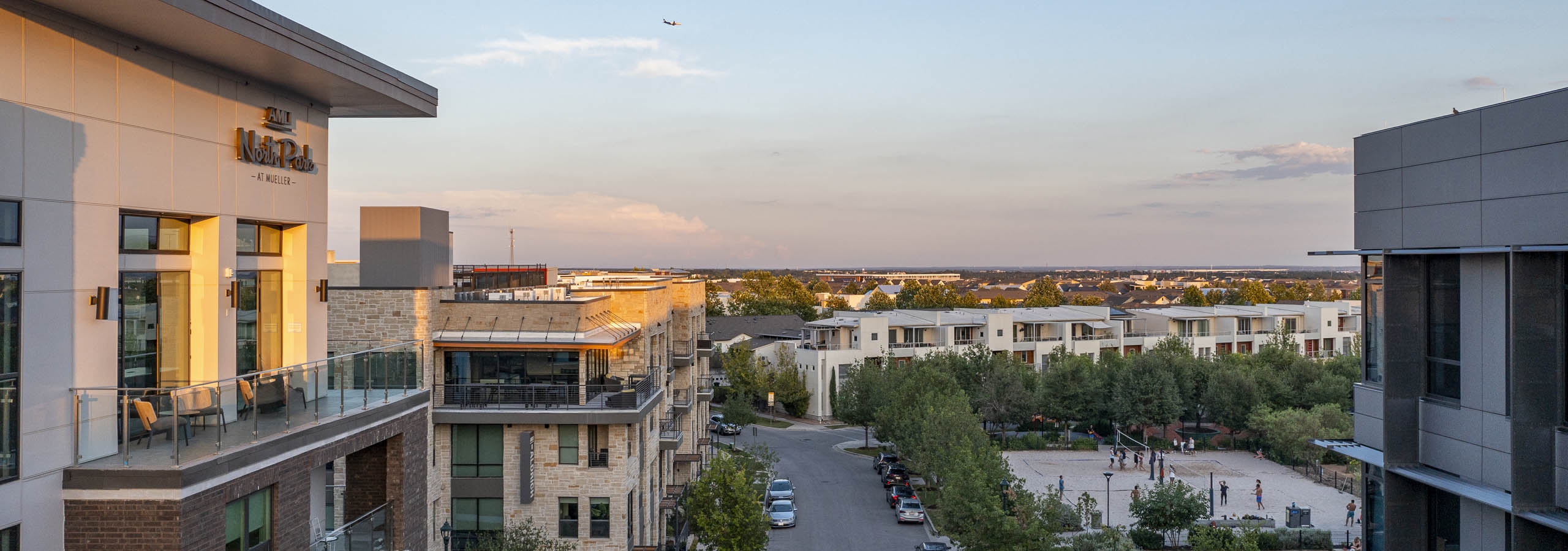 Sunset view of AMLI North Park apartment building kitty corner from park with beach volleyball court and tree lined sidewalks