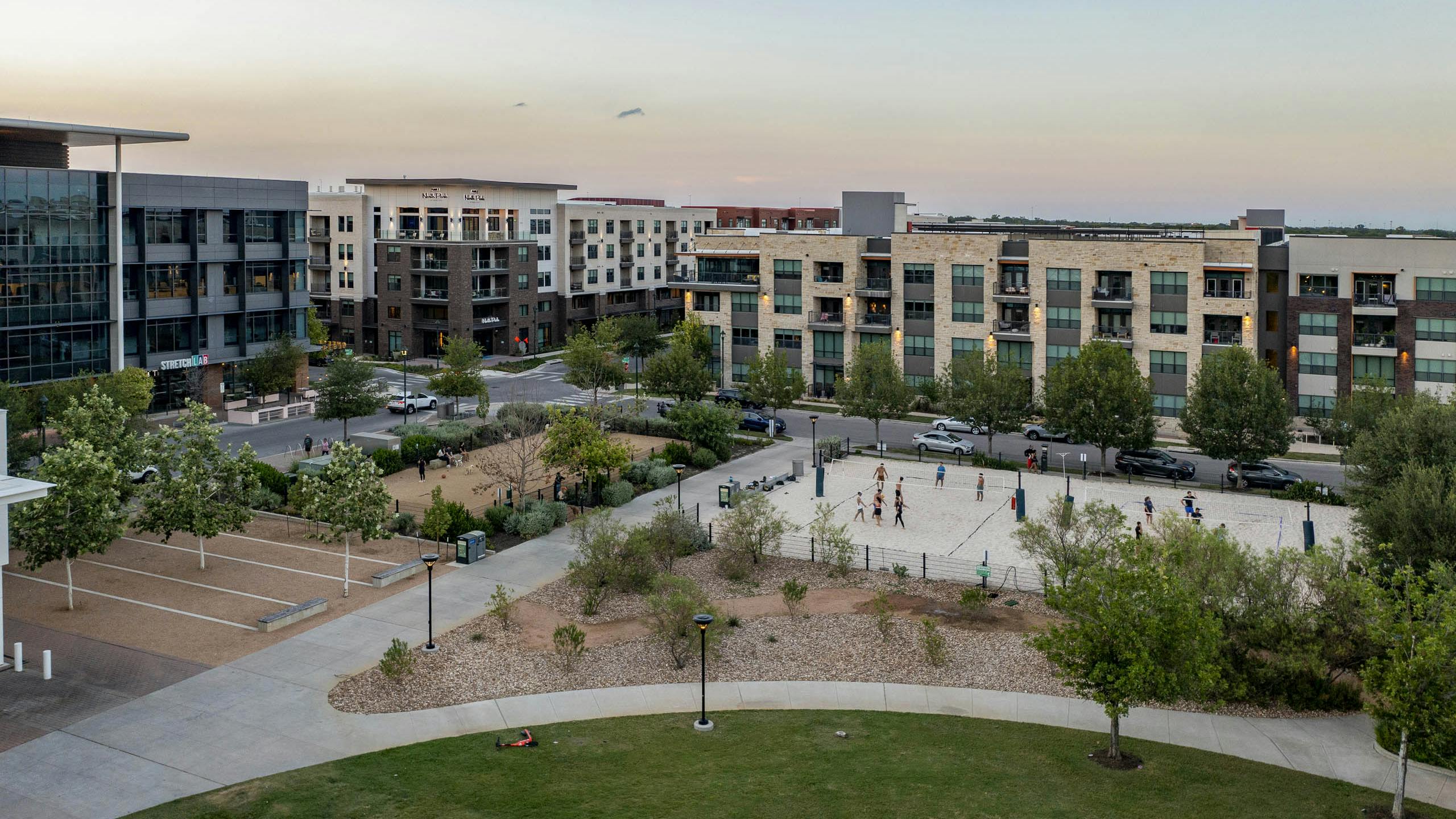 Aerial view of AMLI North Park apartments at sunset overlooking Elizabeth Mary Branch Park with a dog park and volleyball court
