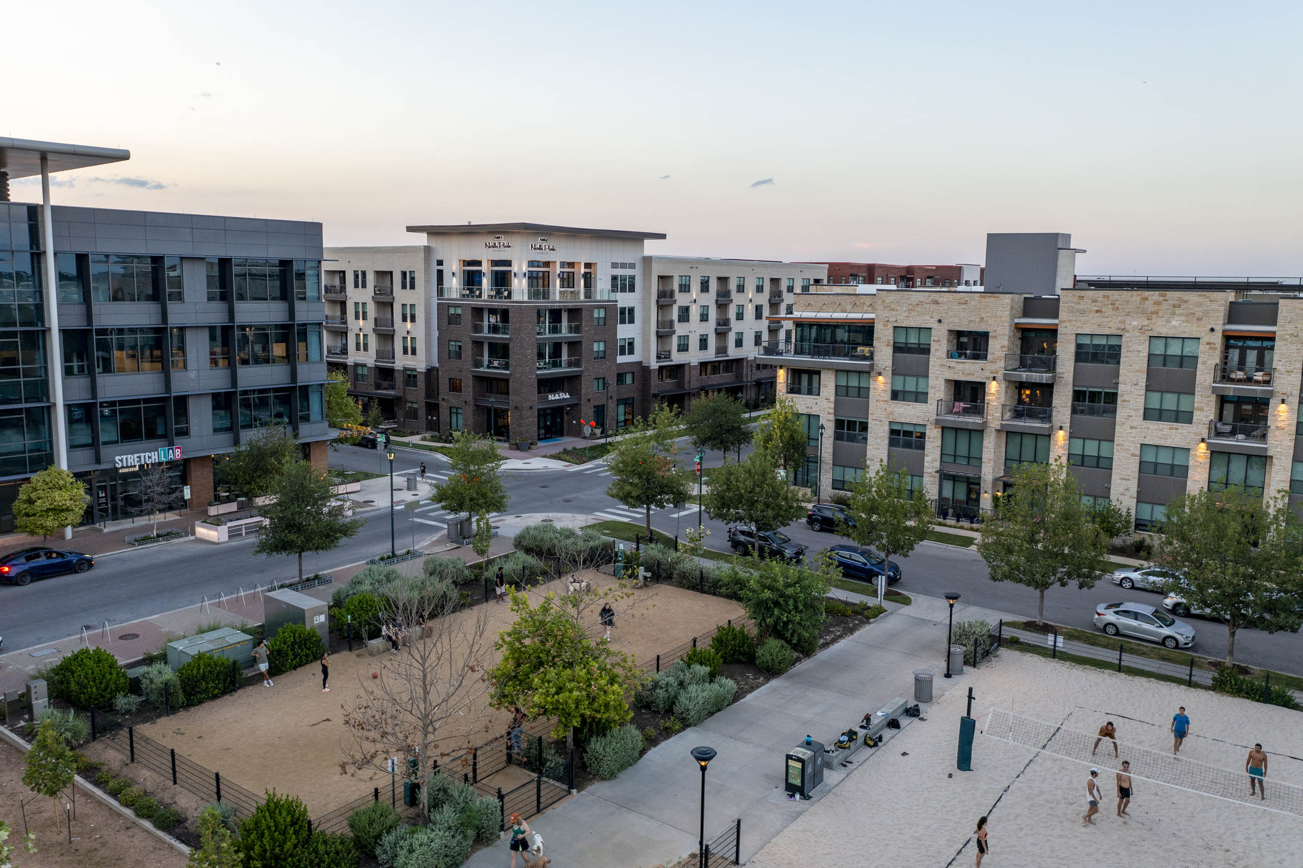 Aerial view of AMLI North Park apartments at sunset overlooking Elizabeth Mary Branch Park with a dog park and volleyball court