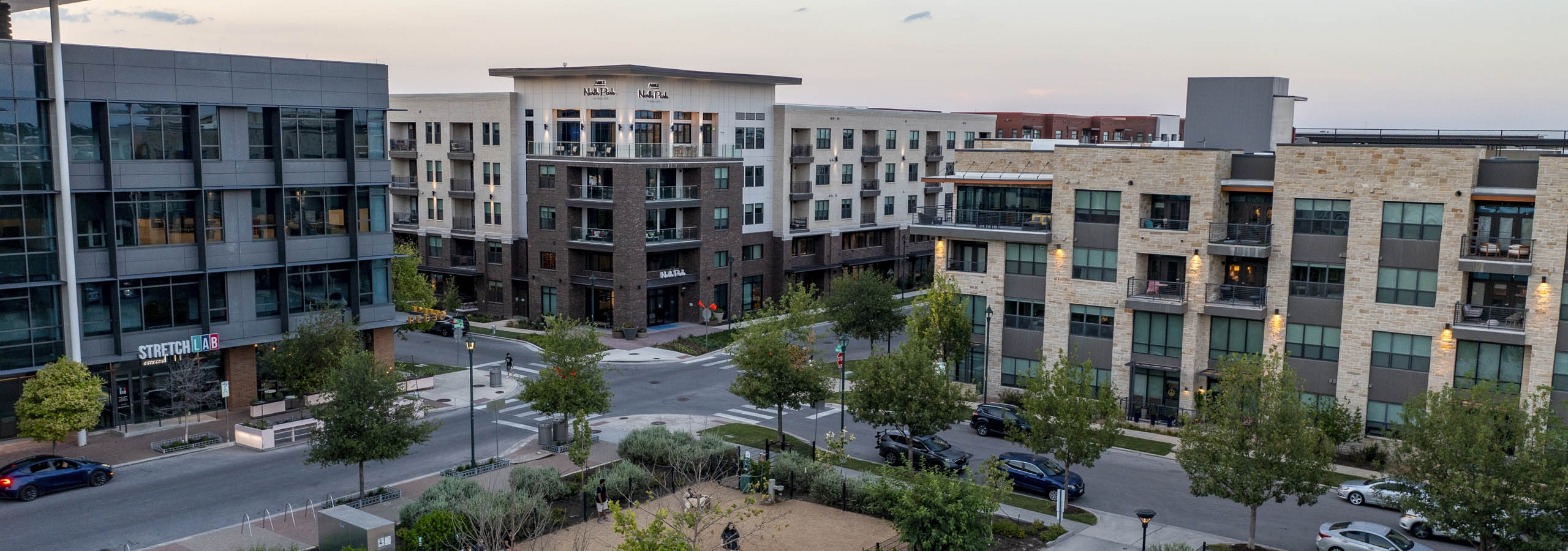 Aerial view of AMLI North Park apartments at sunset overlooking Elizabeth Mary Branch Park with a dog park and volleyball court