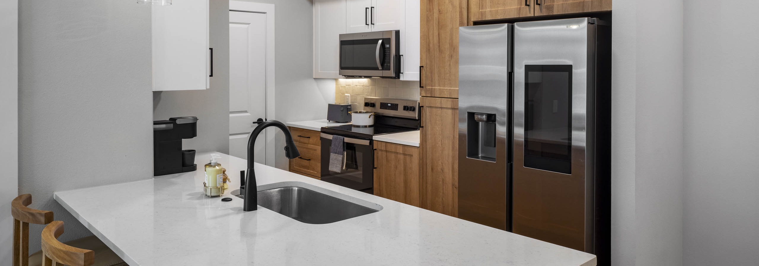 Kitchen interior at AMLI North Park apartment with white island sink pendant lights wood cabinets stainless appliances and bar stools