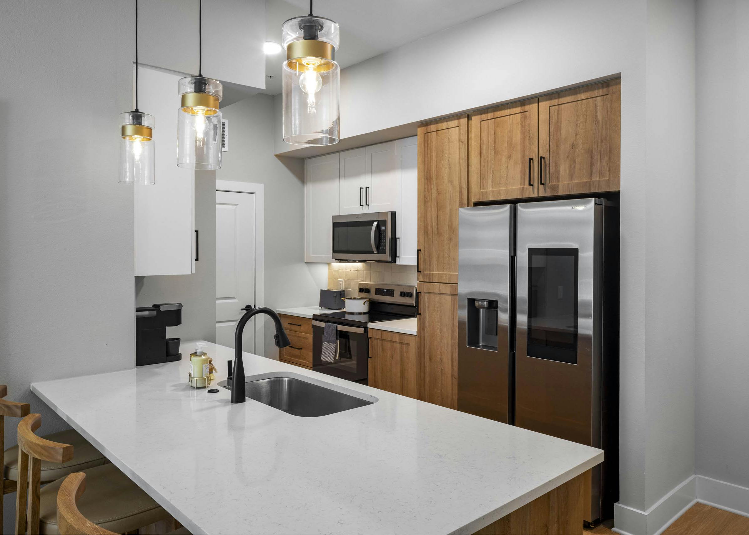 Kitchen interior at AMLI North Park apartment with white island sink pendant lights wood cabinets stainless appliances and bar stools