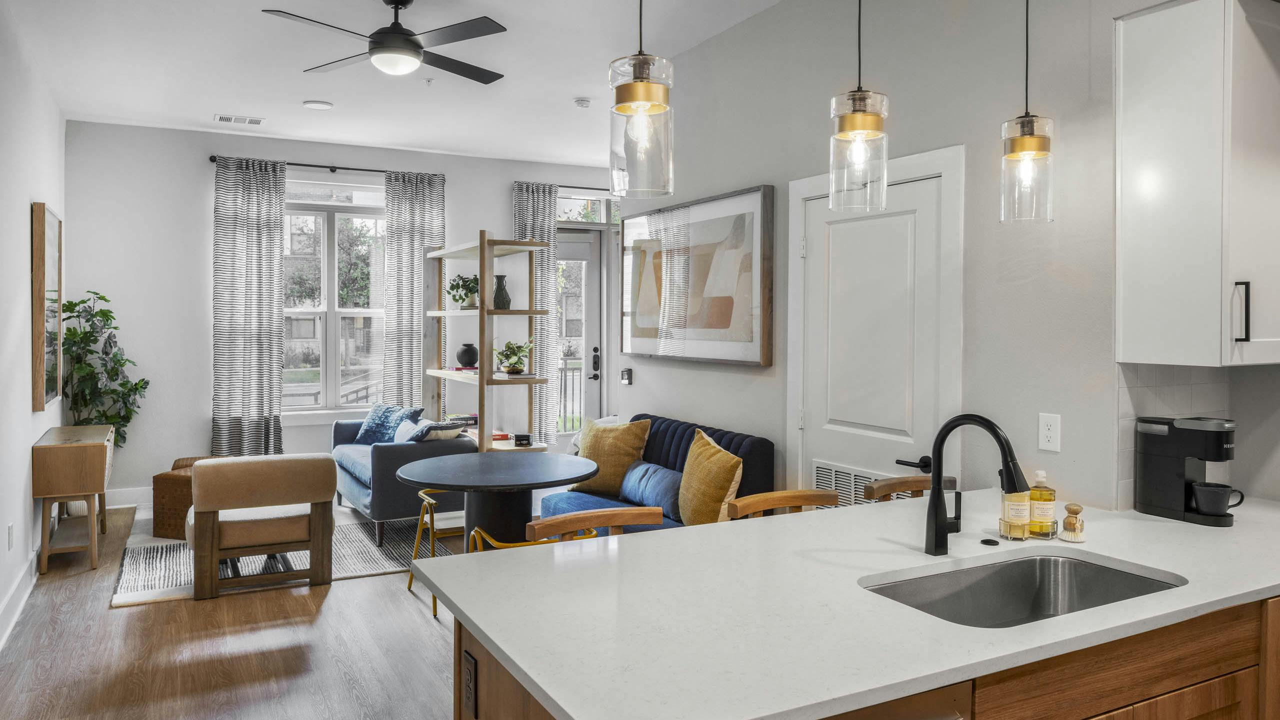 Open concept AMLI North Park apartment interior with kitchen white countertop pendant lights blue sofa yellow pillows and round table
