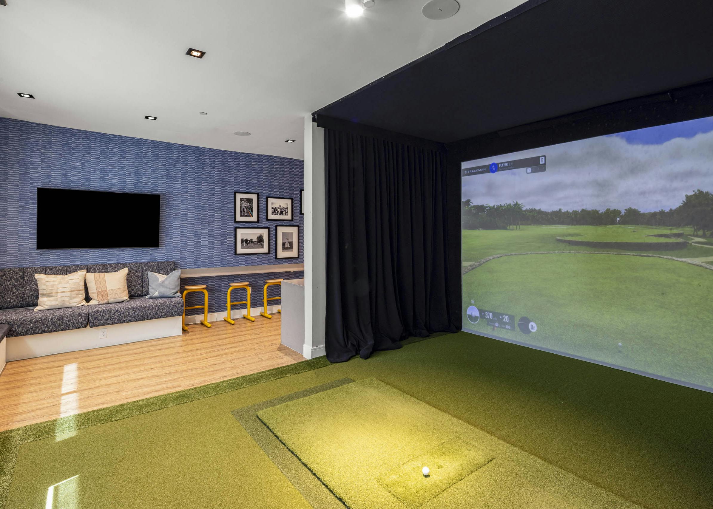 Indoor golf simulator room at AMLI North Park apartment community with screen turf mat bench seating yellow stools and wall décor