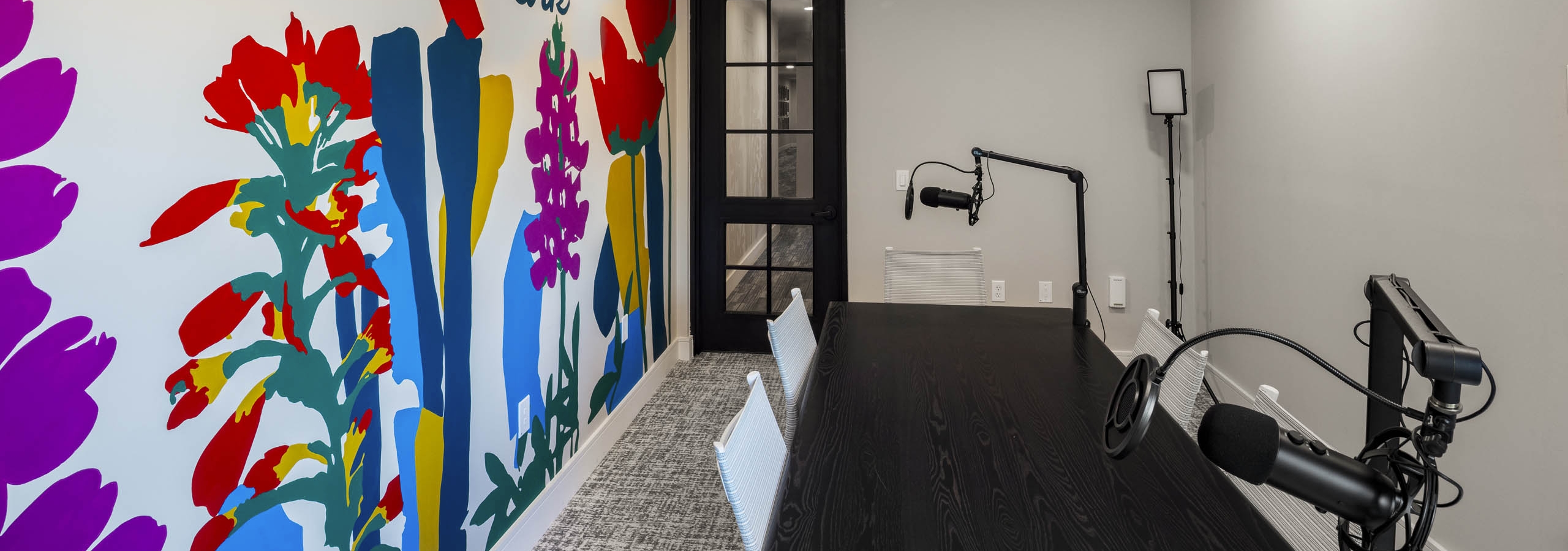 Podcast room at AMLI North Park apartment community with black table white chairs colorful mural microphones and glass door