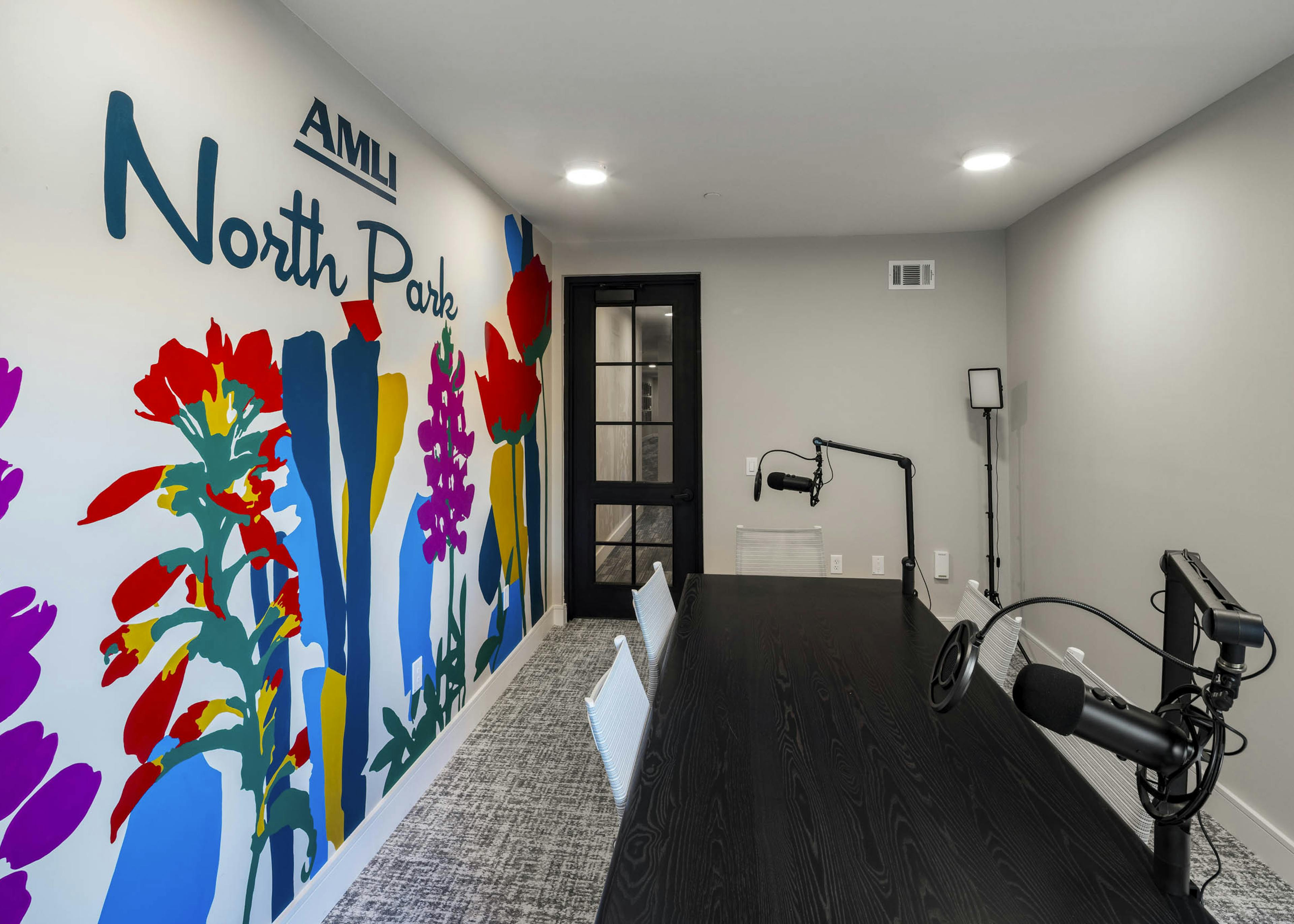Podcast room at AMLI North Park apartment community with black table white chairs colorful mural microphones and glass door